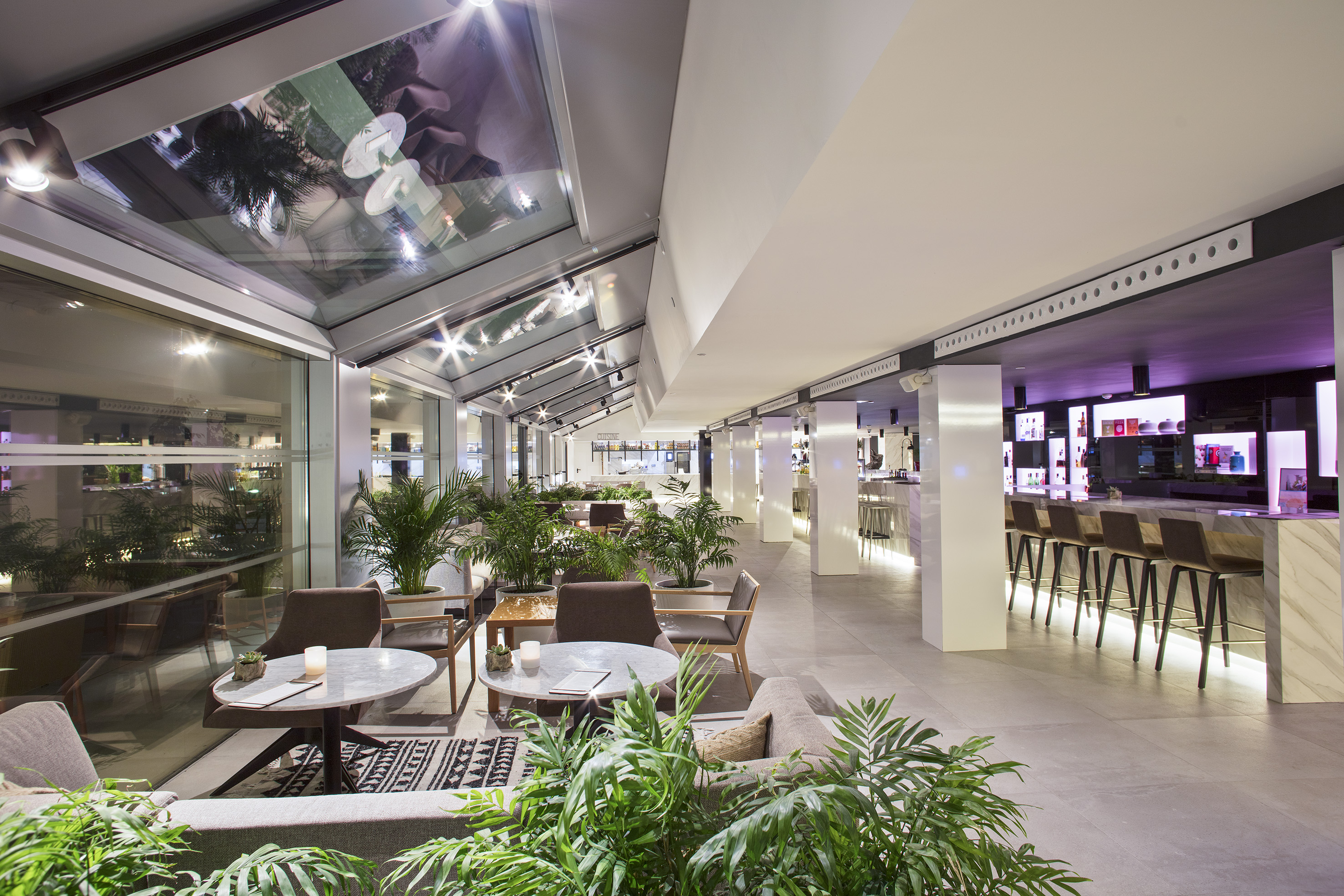 Contemporary hotel lobby bar and lounge with skylight and lush plants.