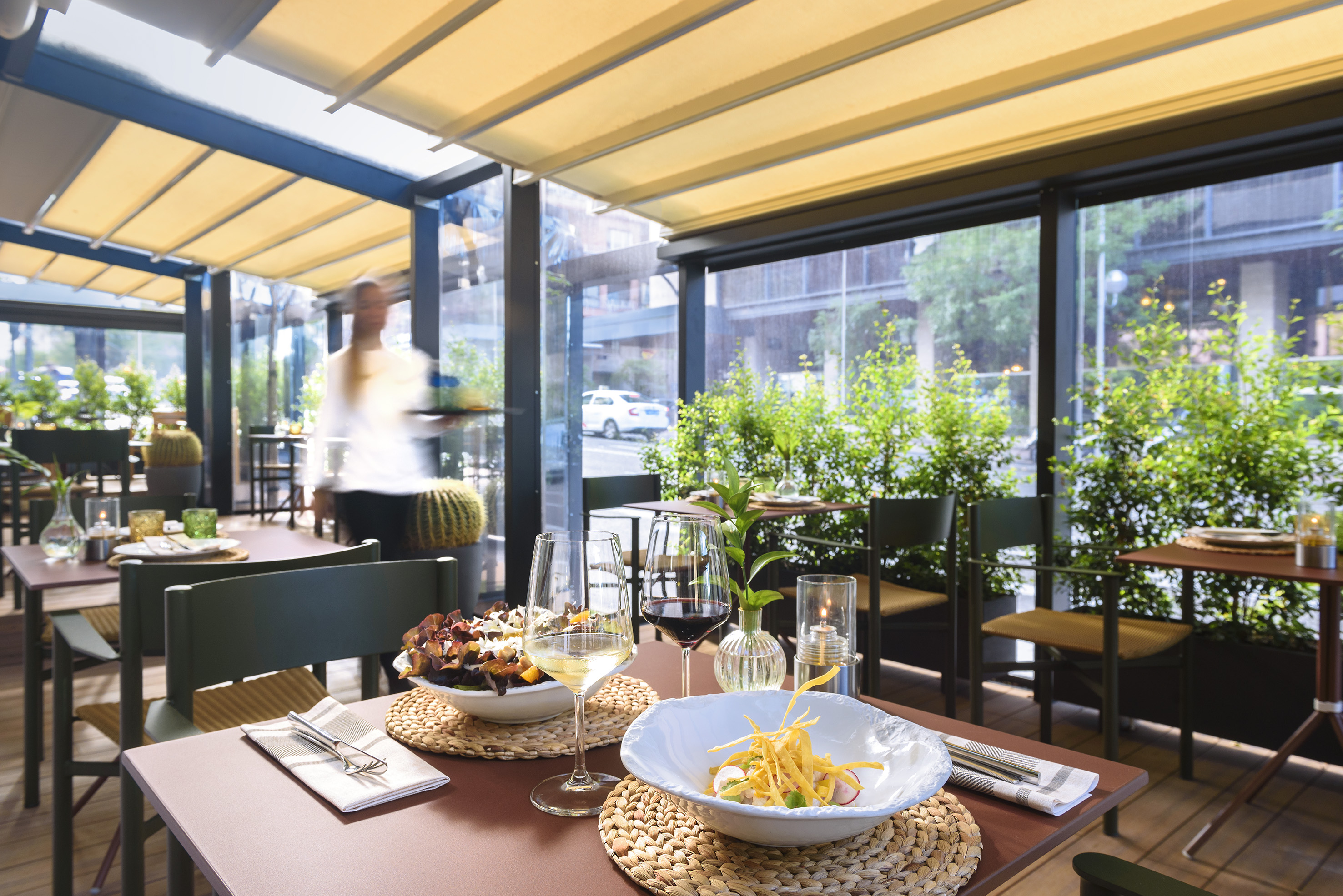 Restaurant terrace with dining tables, wine, food, and retractable canopy.