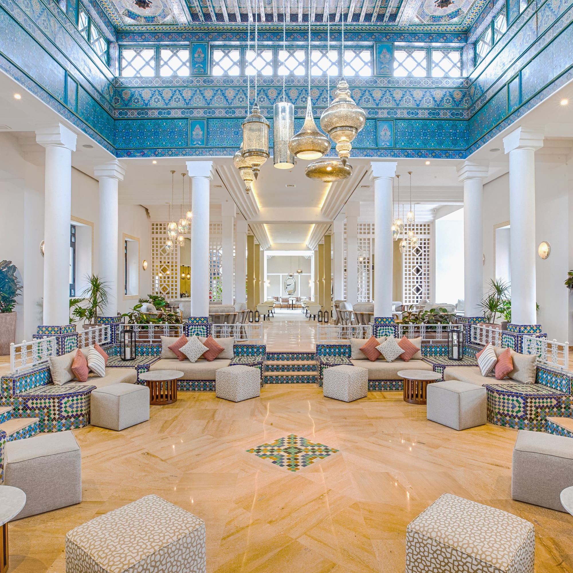 Grand Moroccan lobby with ornate blue tiles, golden lanterns, and lounge seating.