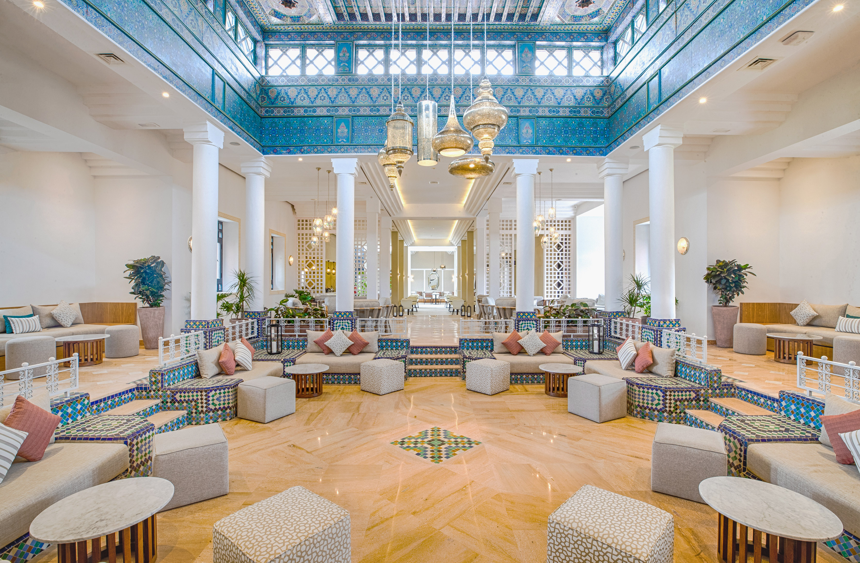 Grand Moroccan lobby with ornate blue tiles, golden lanterns, and lounge seating.
