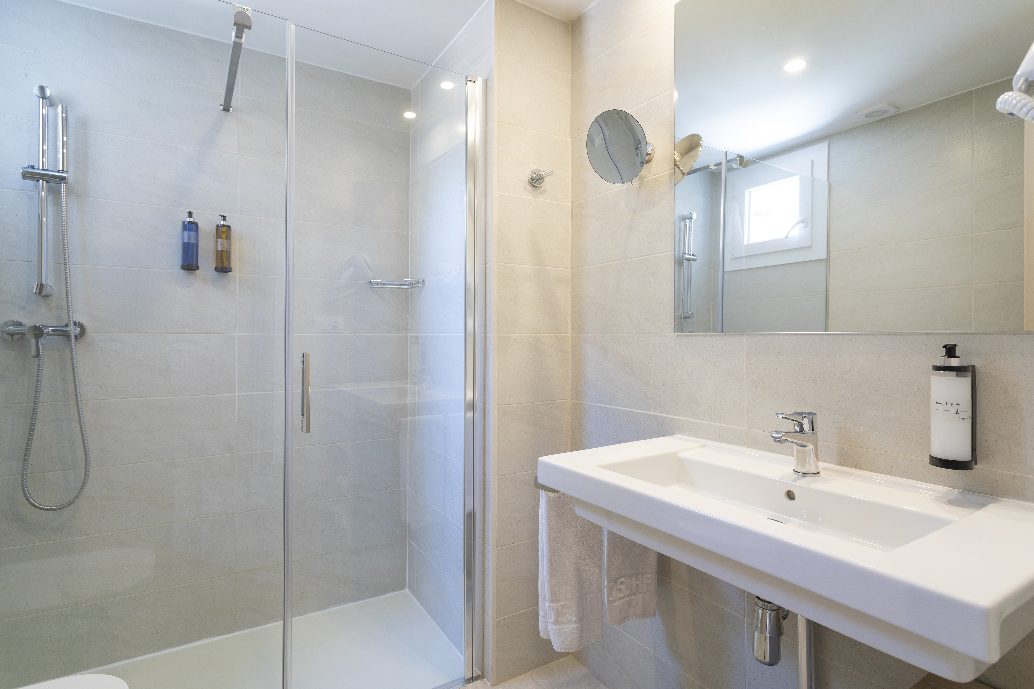 Bright, tiled bathroom with glass walk-in shower, sink, and mirror.