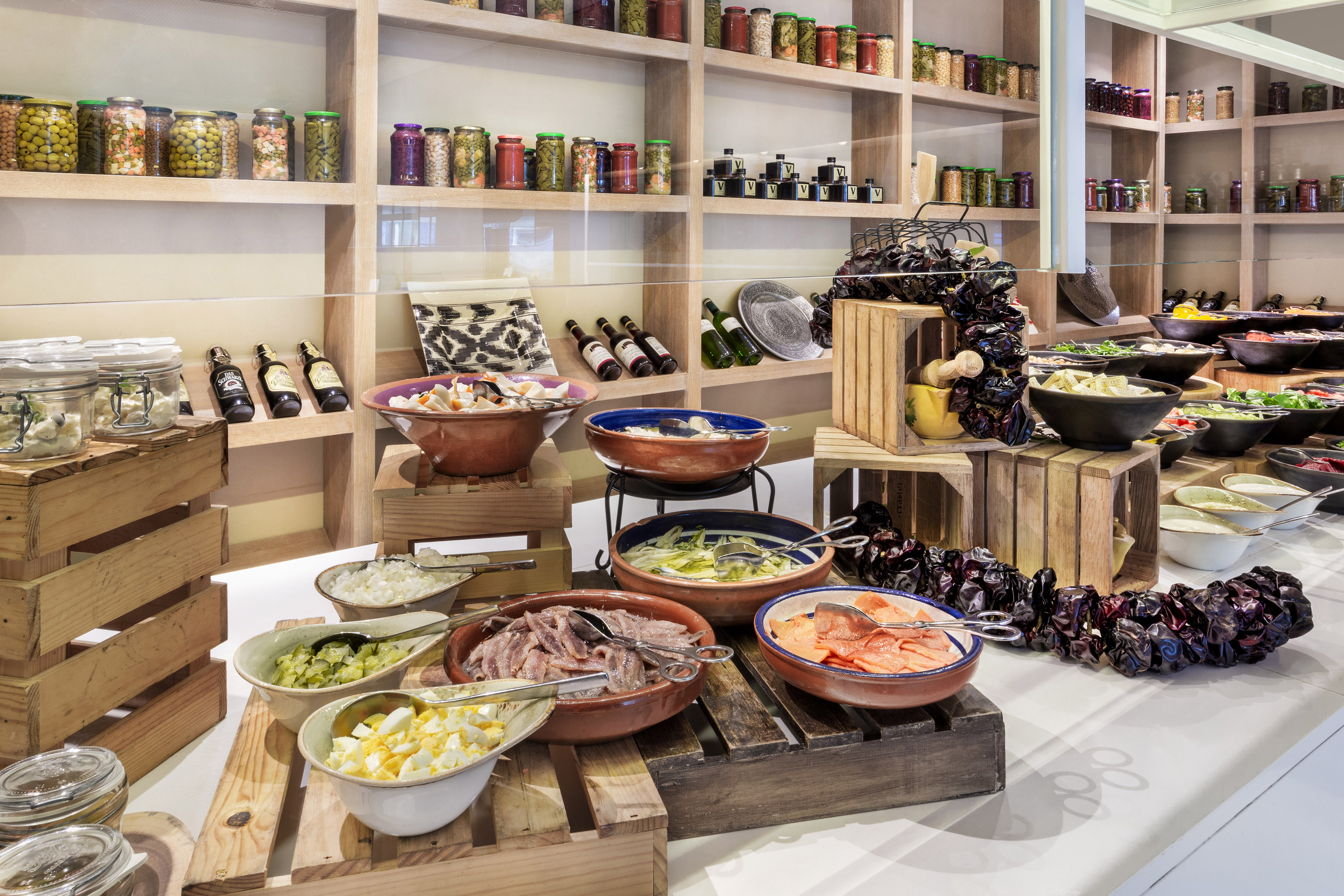 Buffet table with salads, pickled vegetables, anchovies, and jars of preserves.