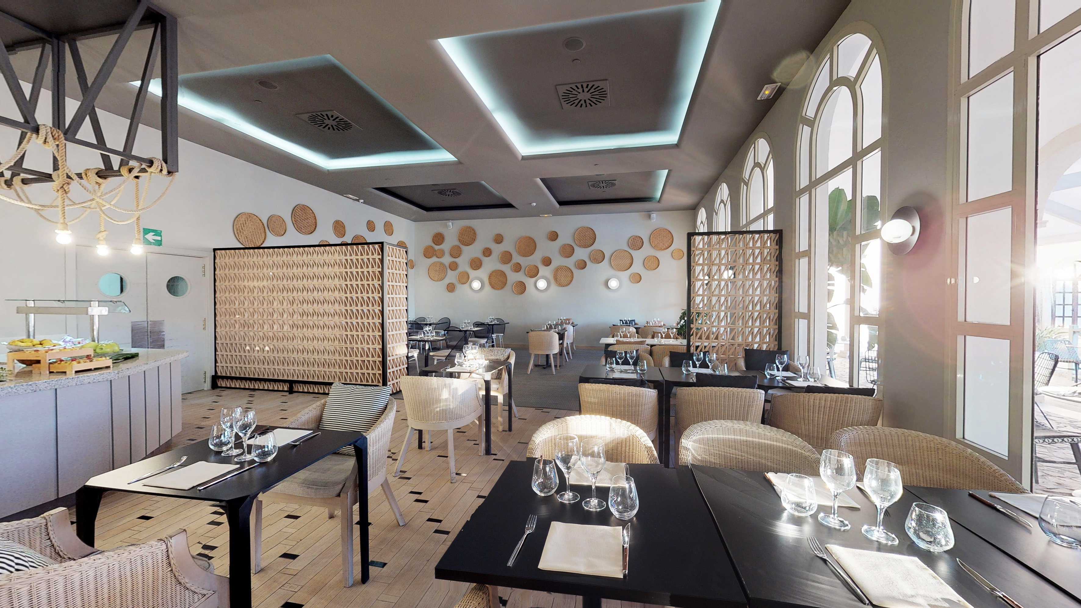 Modern restaurant interior with wicker chairs, buffet, and arched windows.