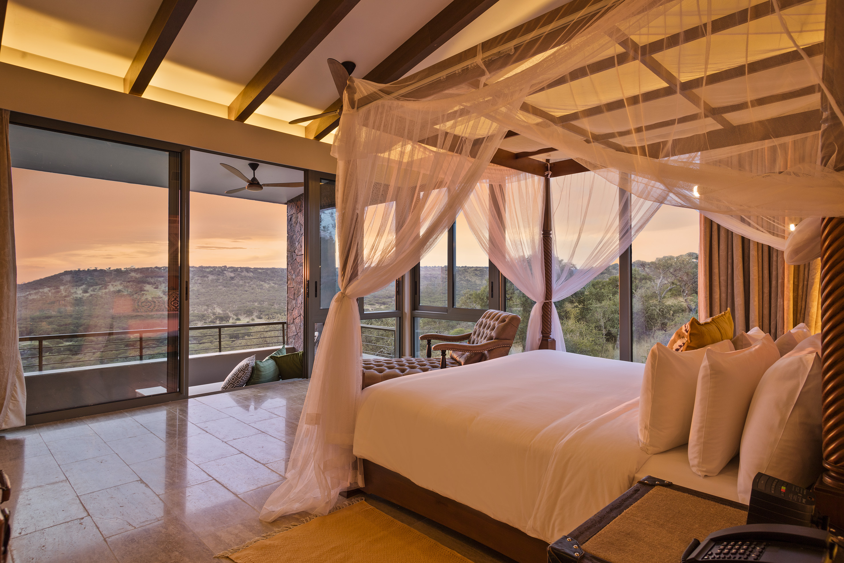 Luxury bedroom with four-poster bed, mosquito net, and sunset safari view.