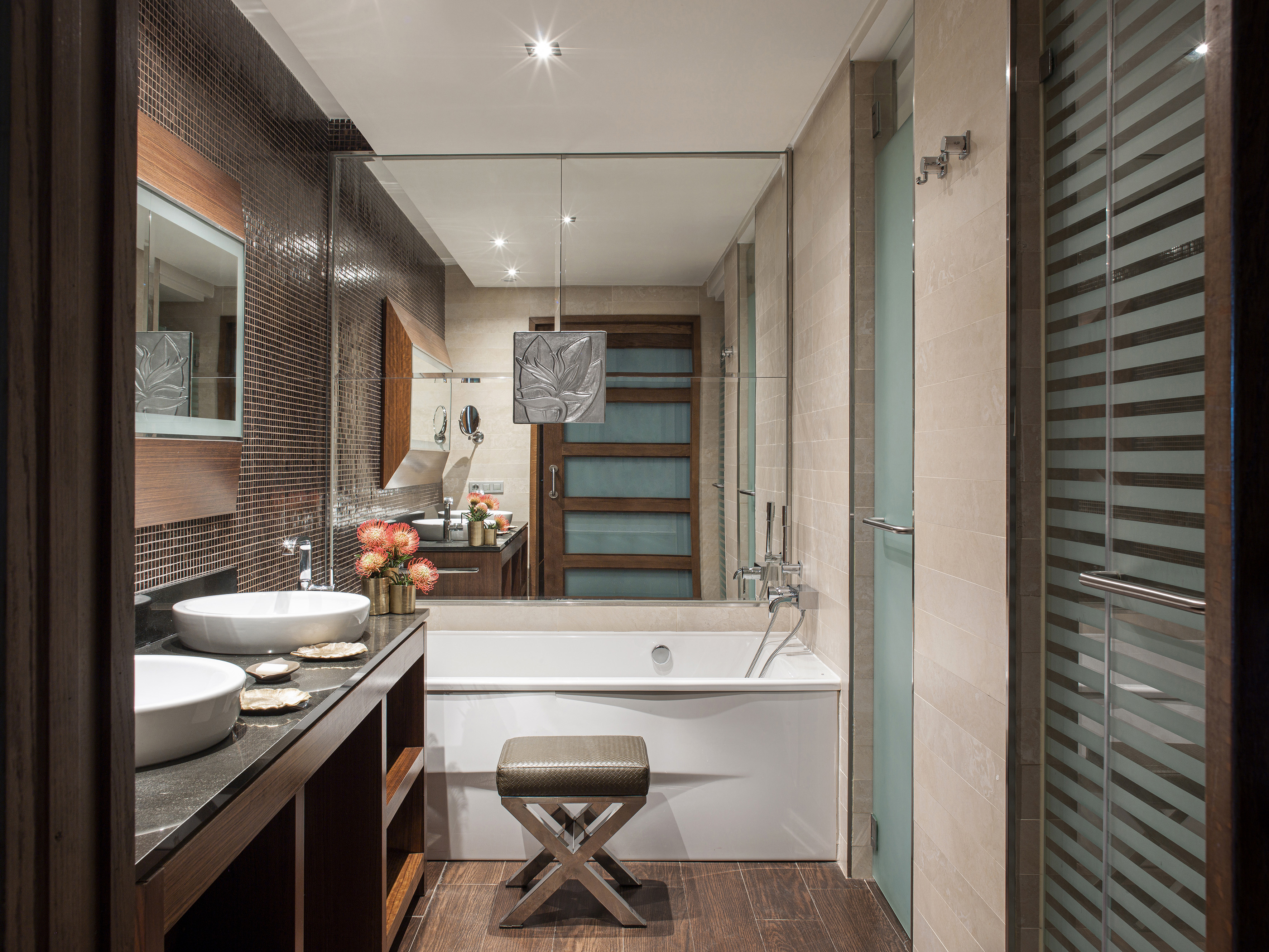 Modern bathroom with double vanity, white bathtub, glass shower, and mosaic wall.