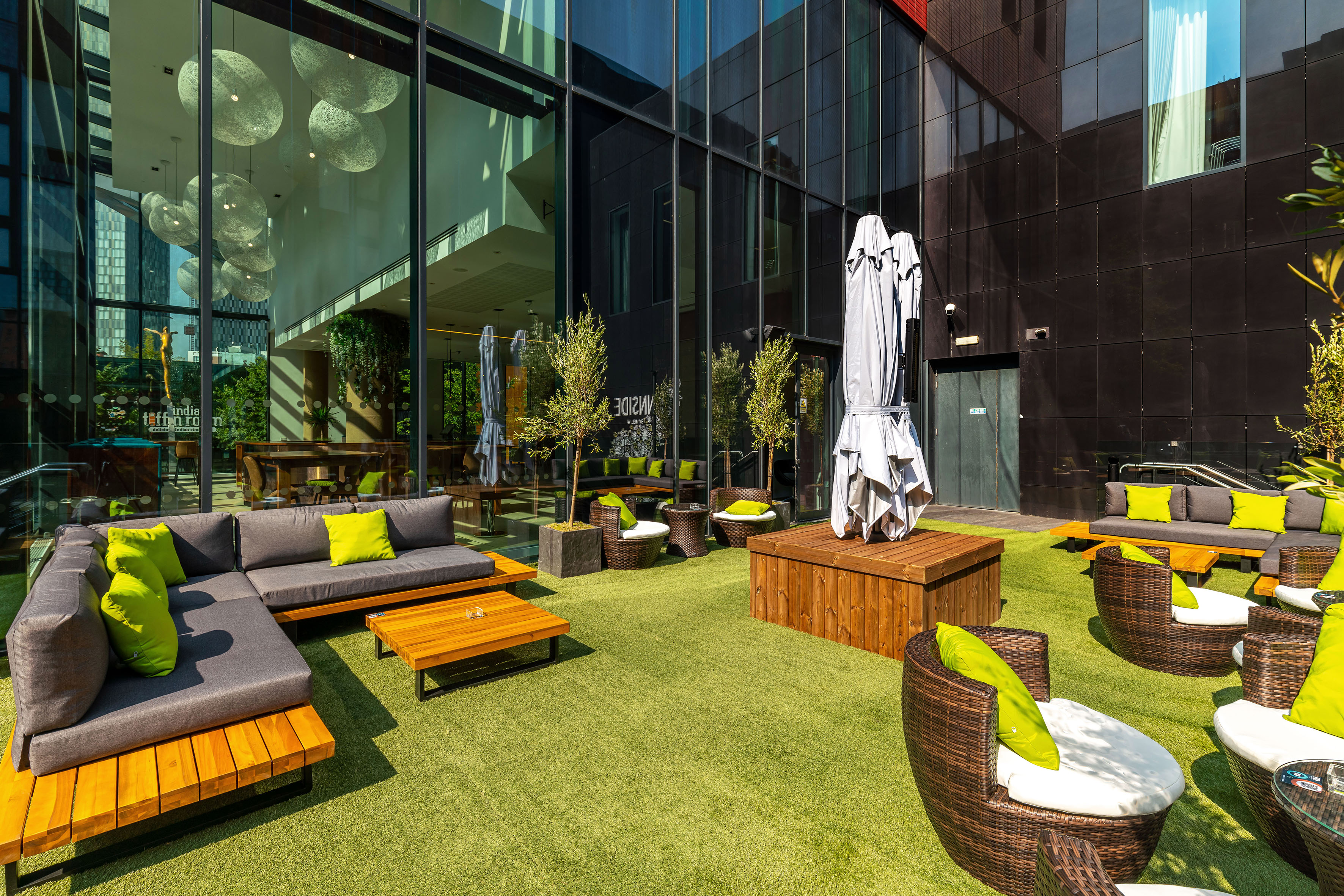 Modern outdoor patio lounge with grey sofas, green pillows, artificial turf.