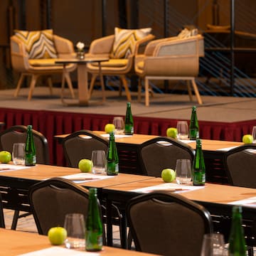 a room with tables and chairs and a stage with chairs and a stage with chairs and a table with green bottles and apples