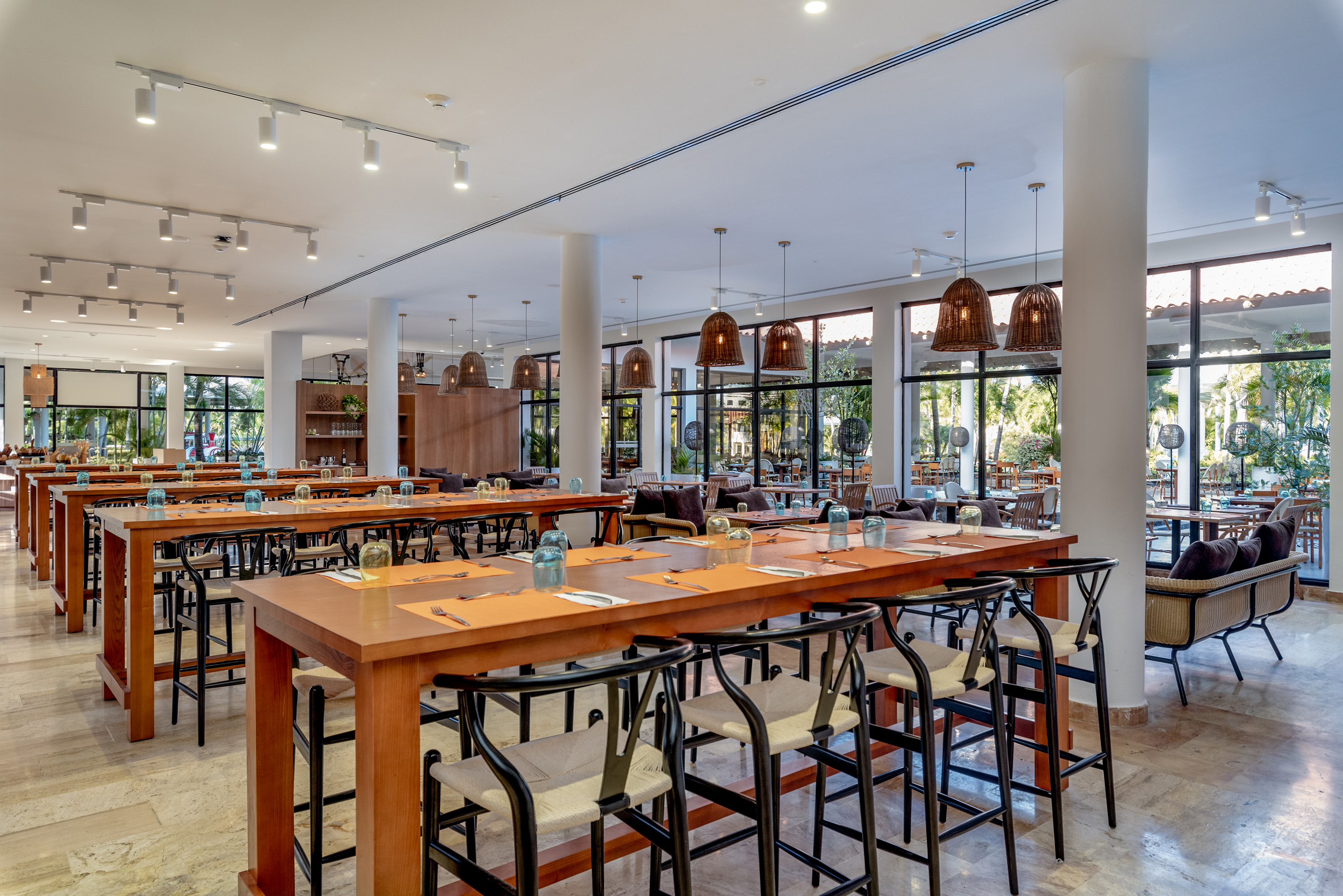 Modern restaurant with high-top wooden tables, bar stools, and tropical view.