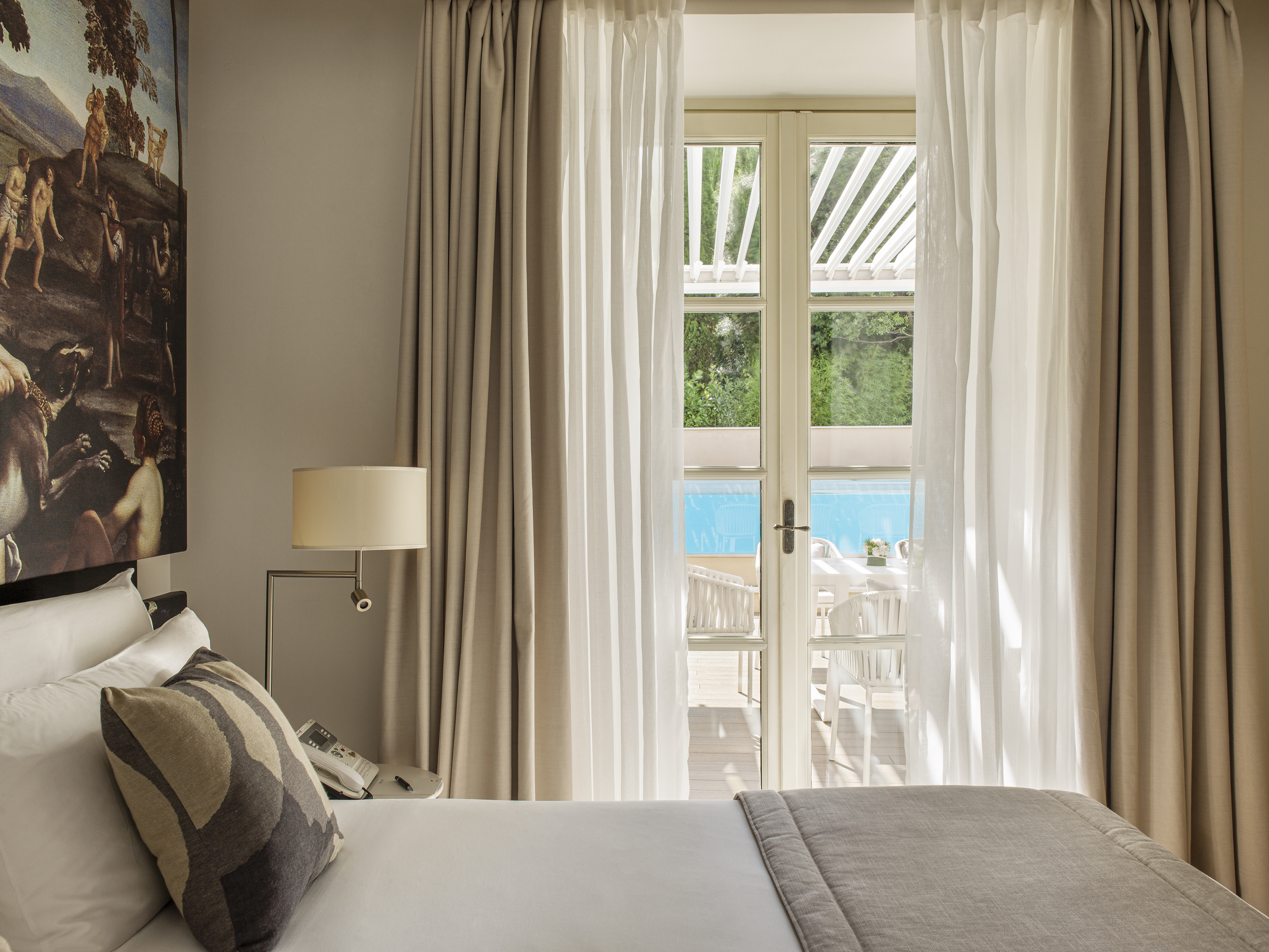Hotel bedroom with open patio doors revealing a swimming pool and terrace.