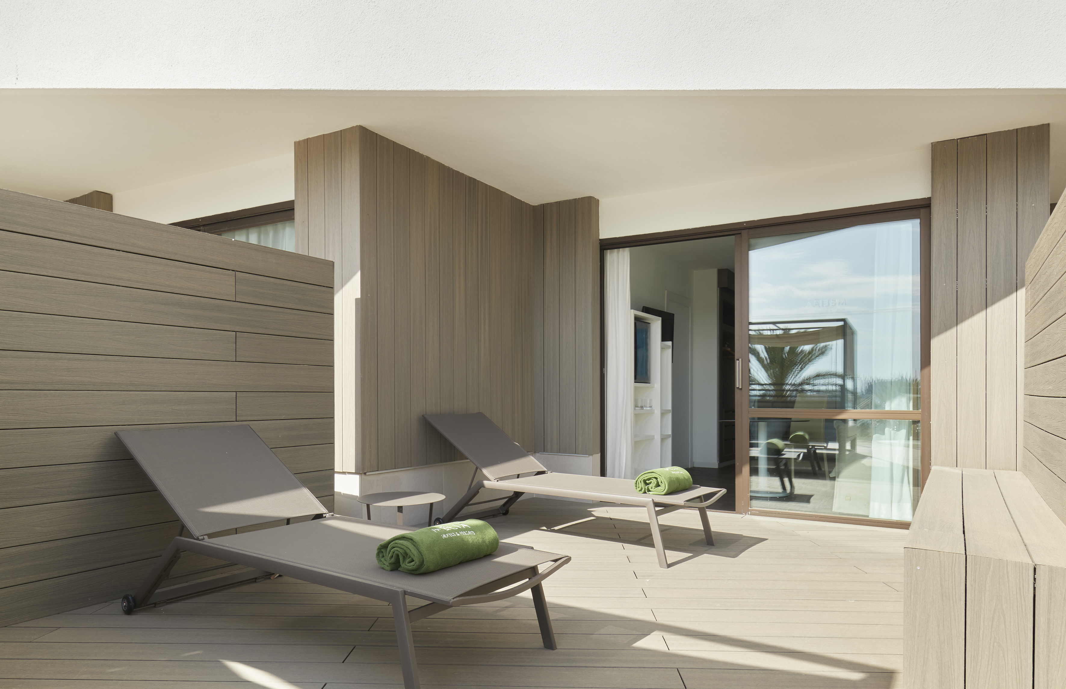 Hotel balcony with two sun loungers, green towels, and wood decking.