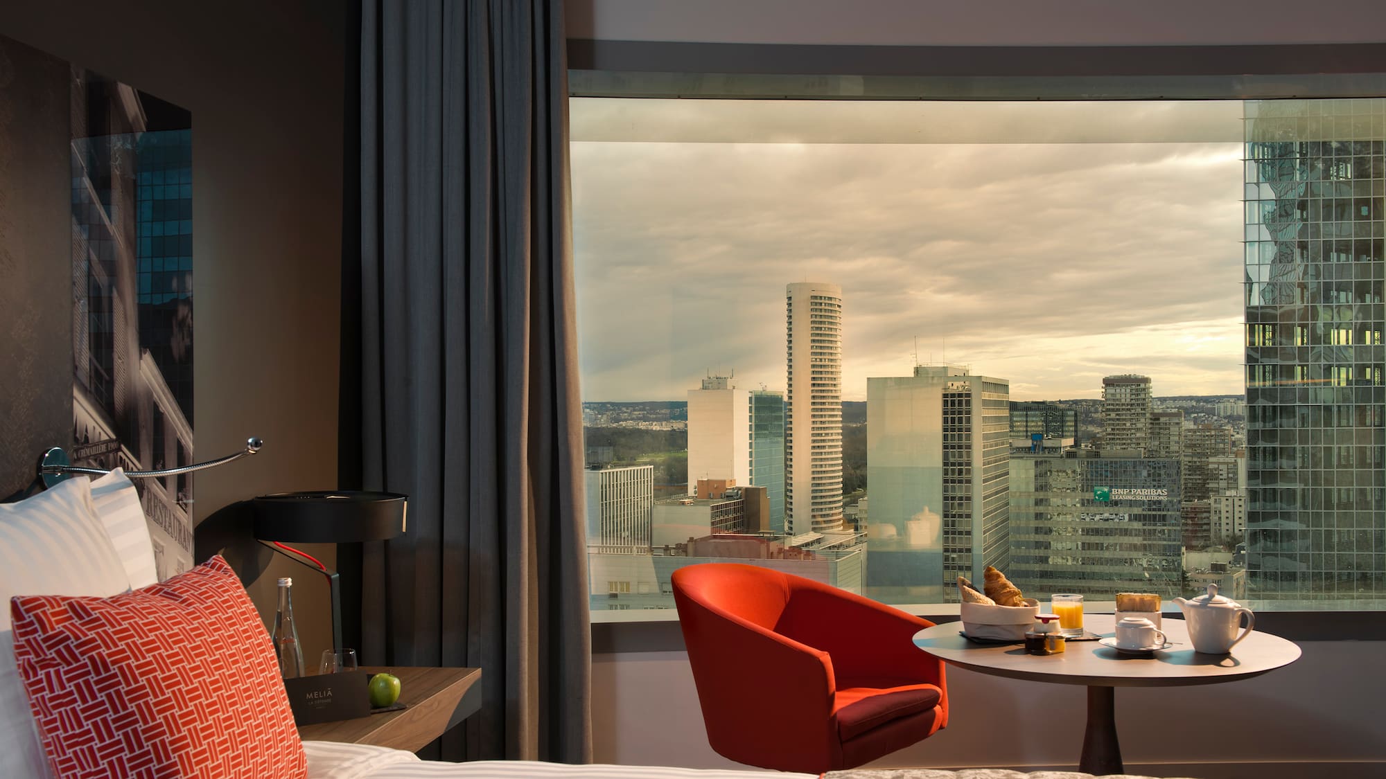 a room with a window and a bed and a table with food and a city view