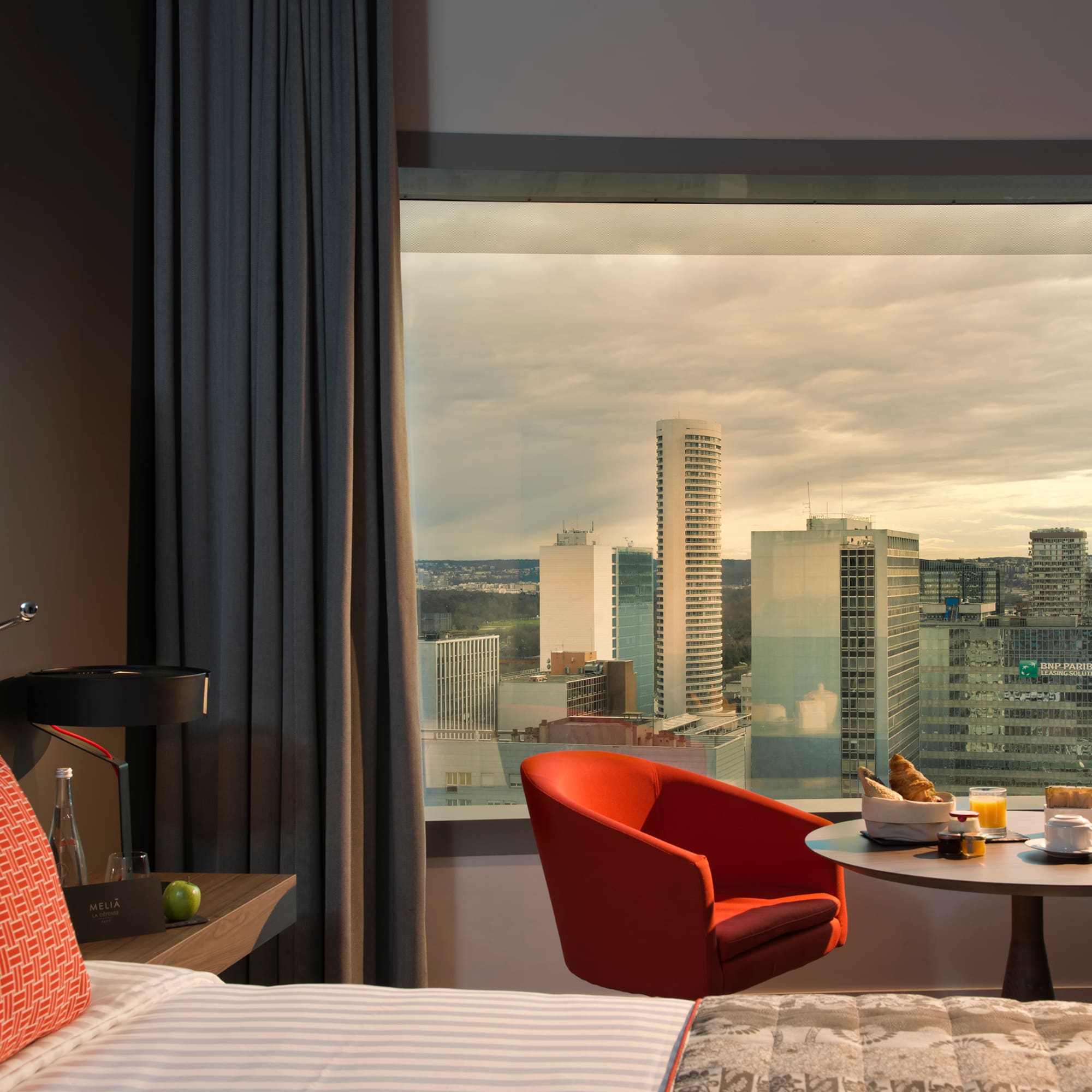 a room with a window and a bed and a table with food and a city view