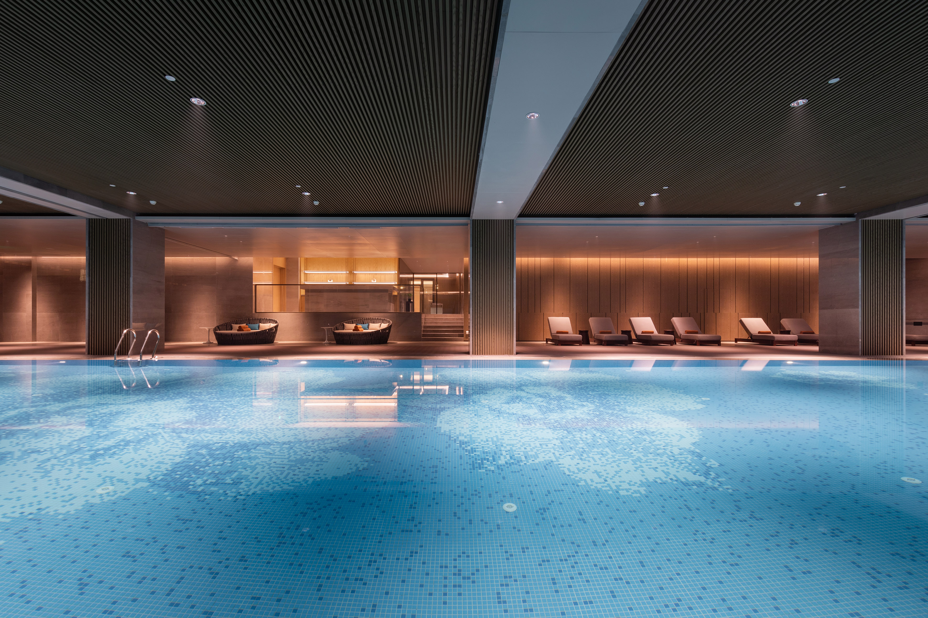 Luxury indoor pool with blue mosaic tiles, warm lighting, and lounge chairs.