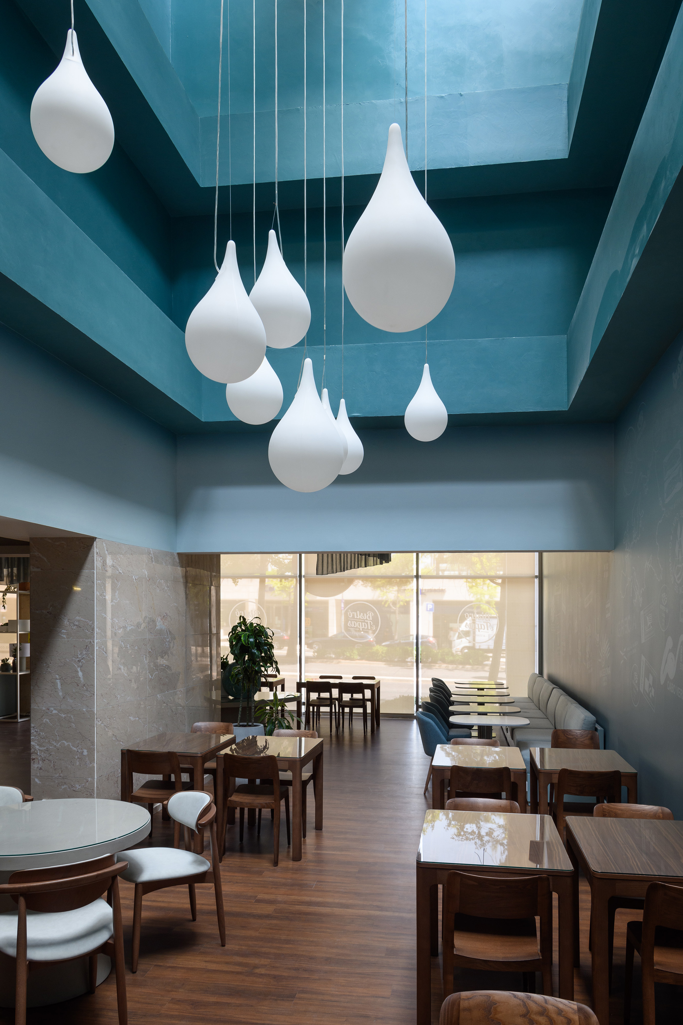 Modern restaurant: blue ceiling, white teardrop pendant lights, wood tables.