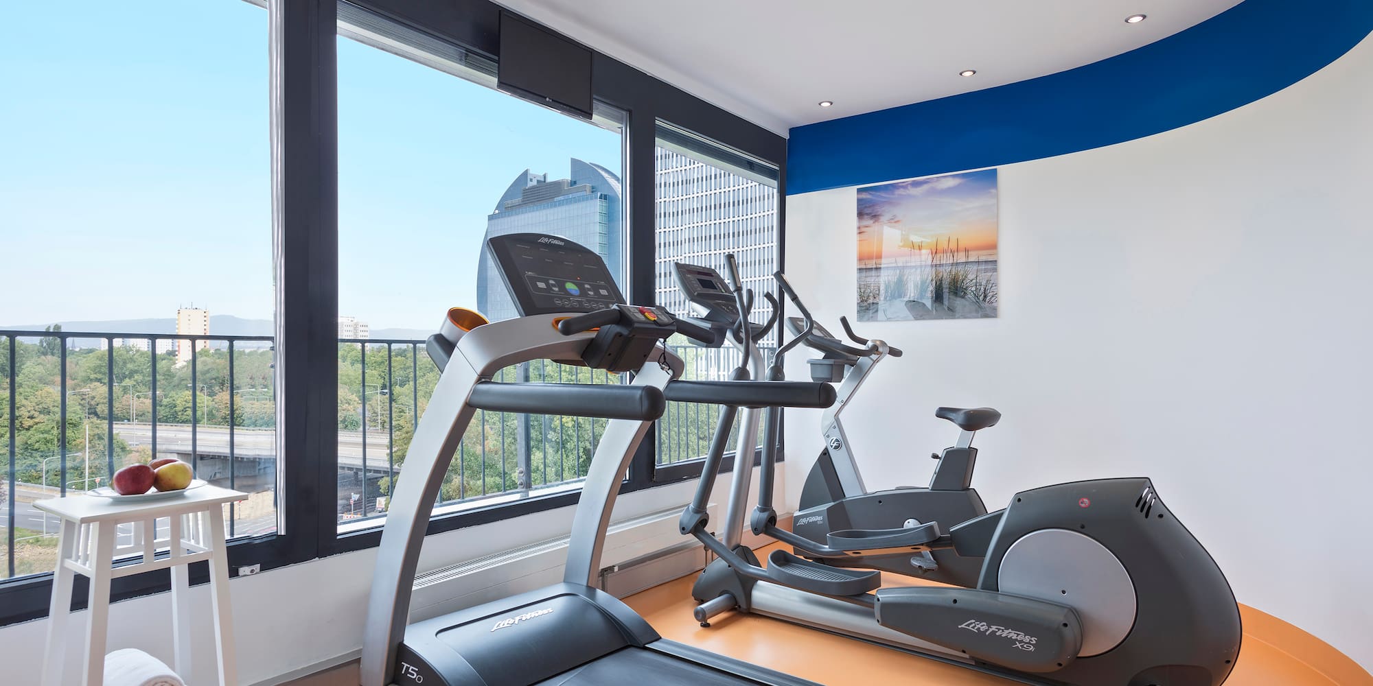 Modern fitness center with treadmill, elliptical, and expansive city views.