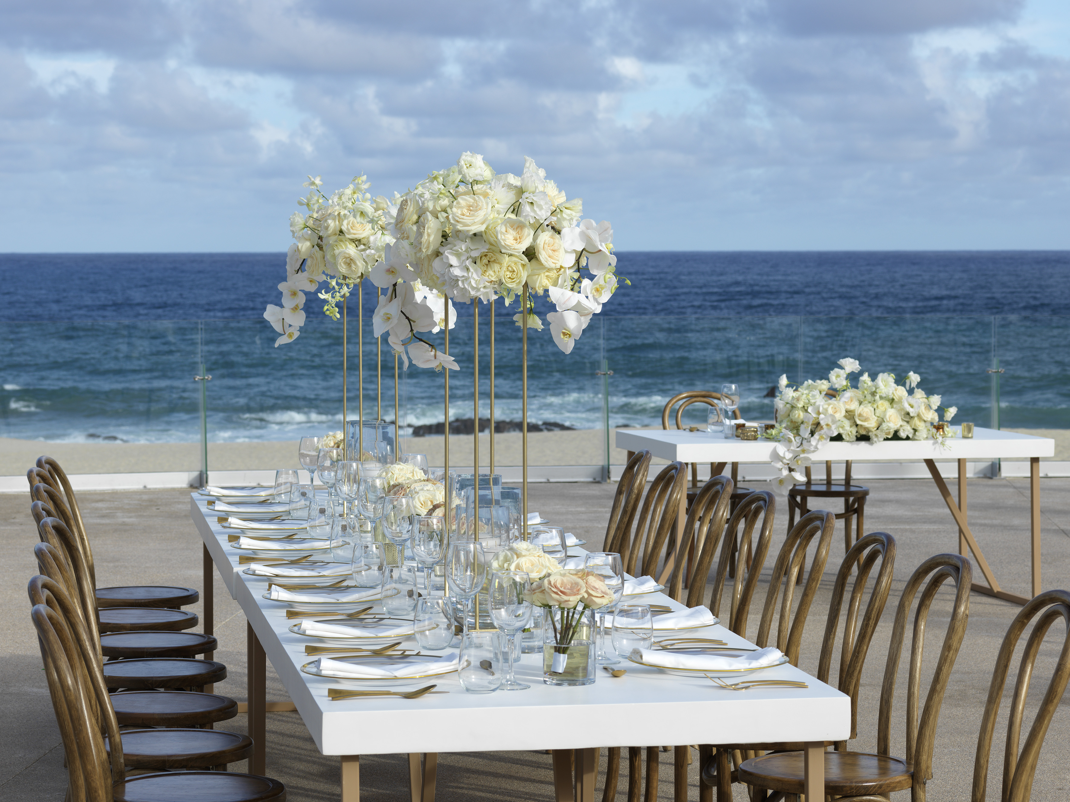 a table set with white flowers and plates on the beach