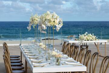 a table set with white flowers and plates on the beach