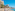 Sunny beach promenade, people, turquoise sea, and cliffside resort hotels.