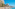 Coastal promenade with beachfront buildings, palm trees, and busy sandy beach.