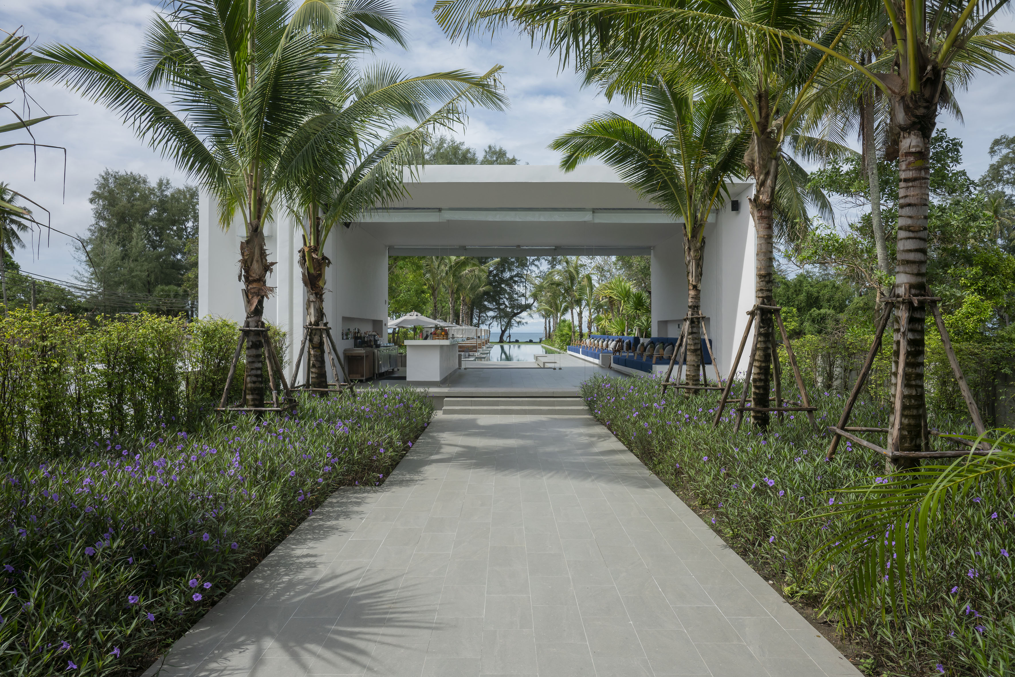 Tiled path to tropical resort pool area with lounge, bar, palm trees, and ocean view.