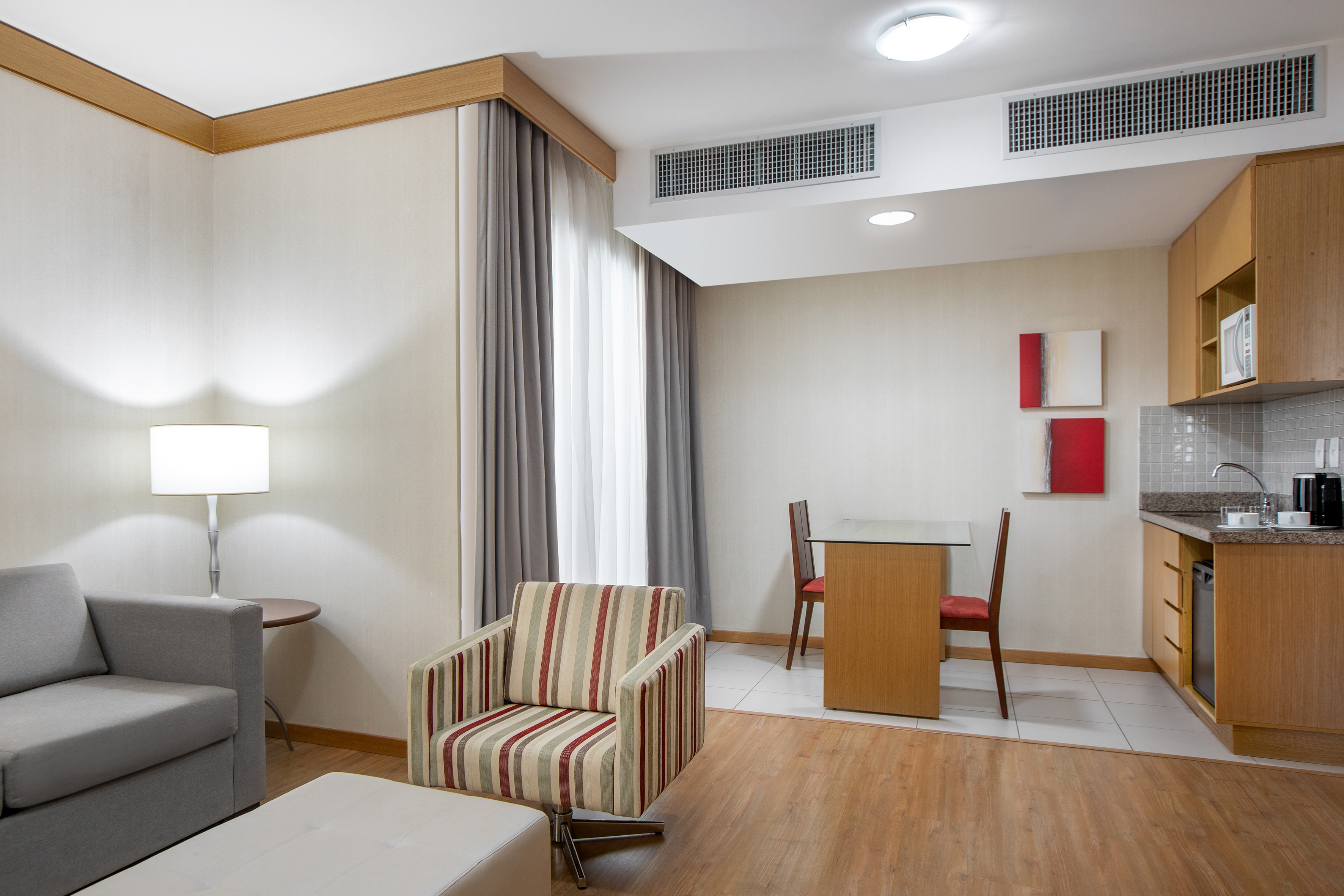Modern hotel suite with living room, compact kitchen, sofa, and dining area.