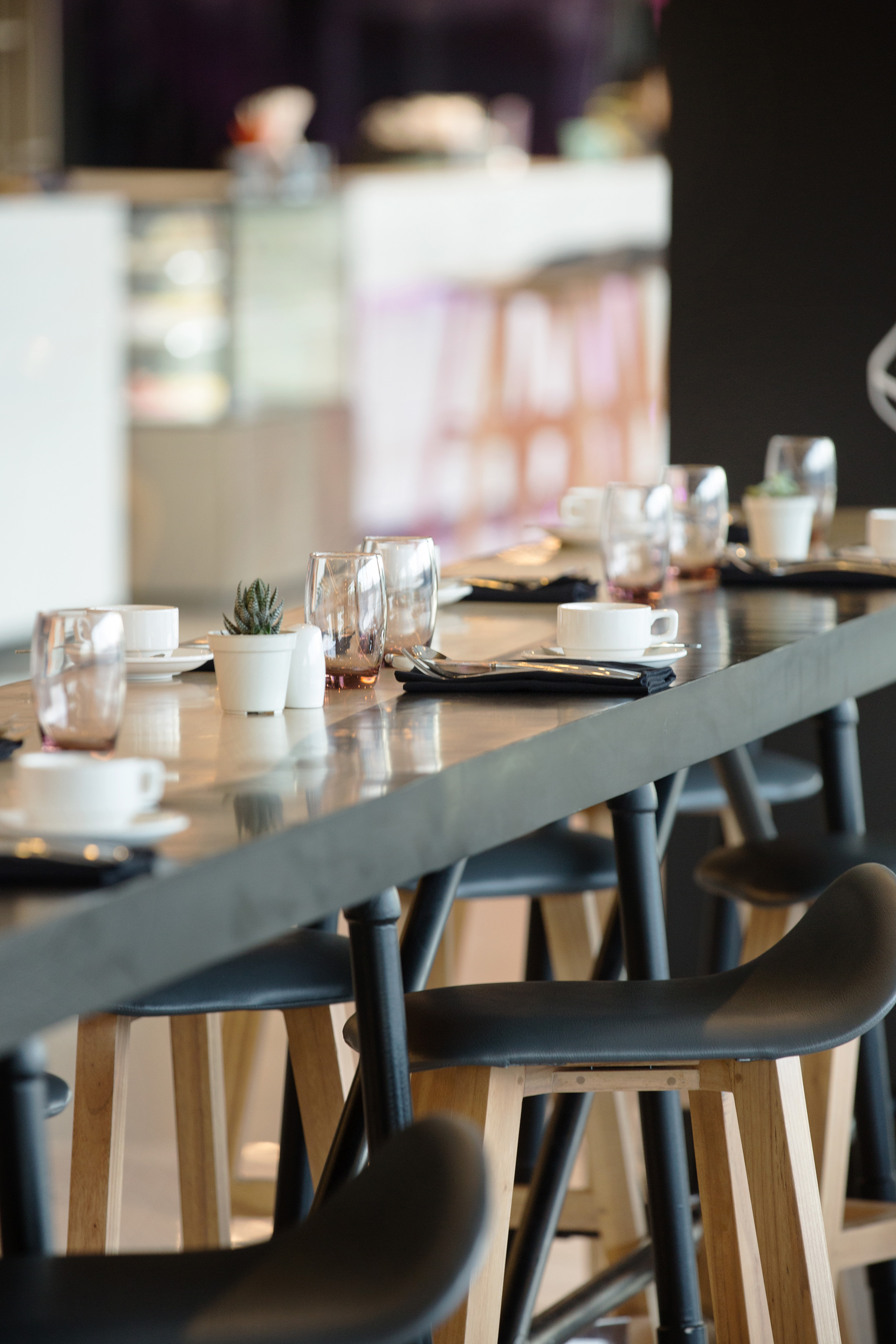 Modern high-top cafe table with coffee cups, glasses, cutlery, and succulents.