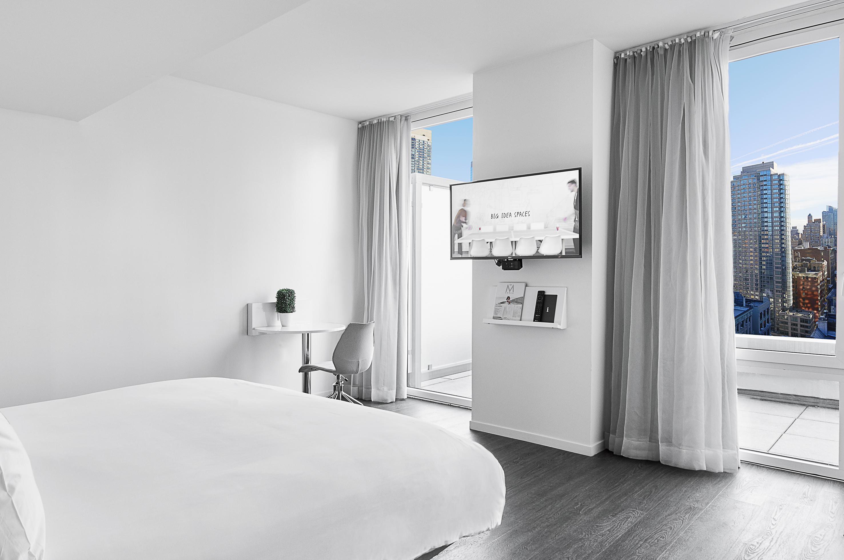 Modern white hotel room with city view, large windows, and wall TV.