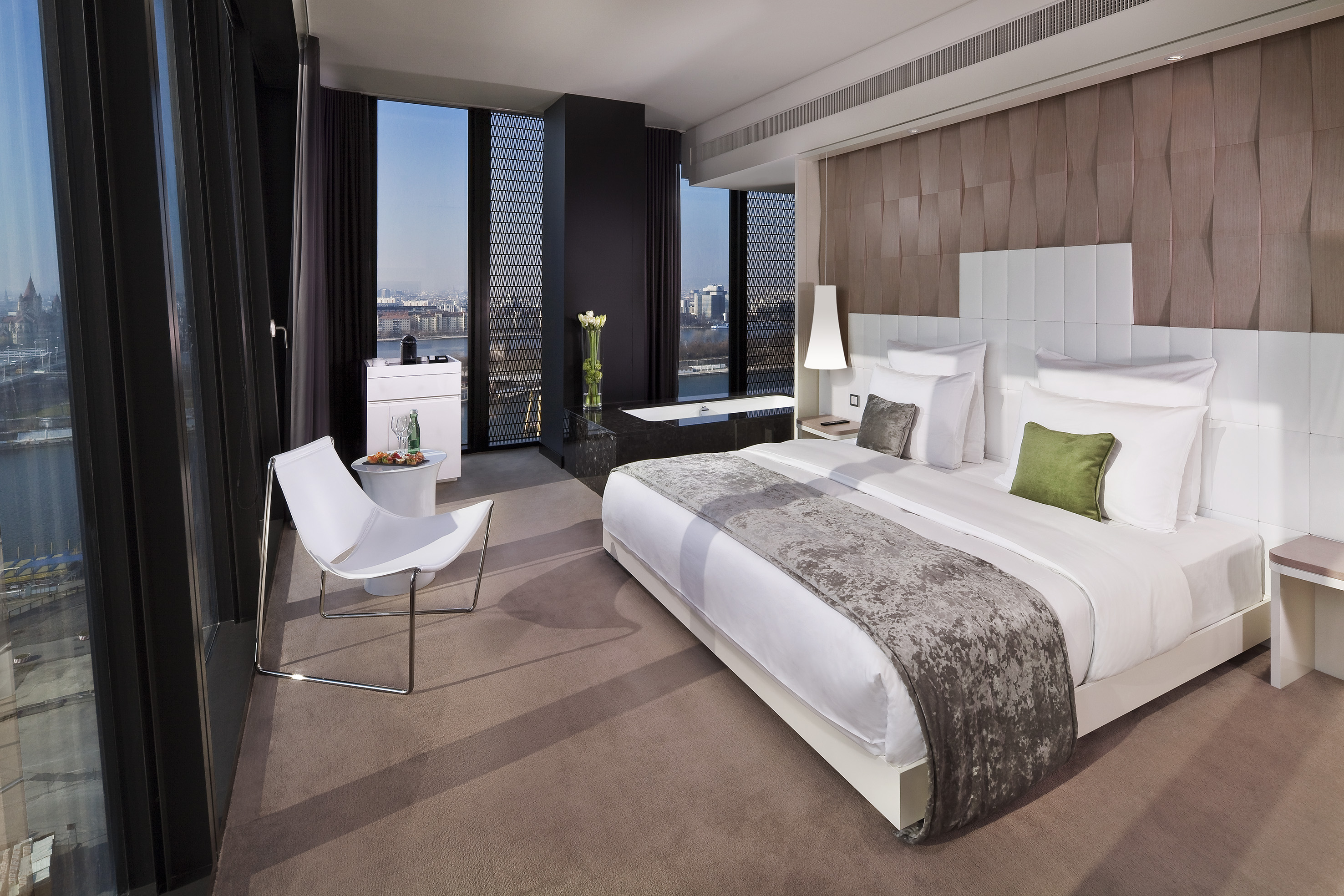 Modern luxury hotel suite with city skyline view and spa bathtub.