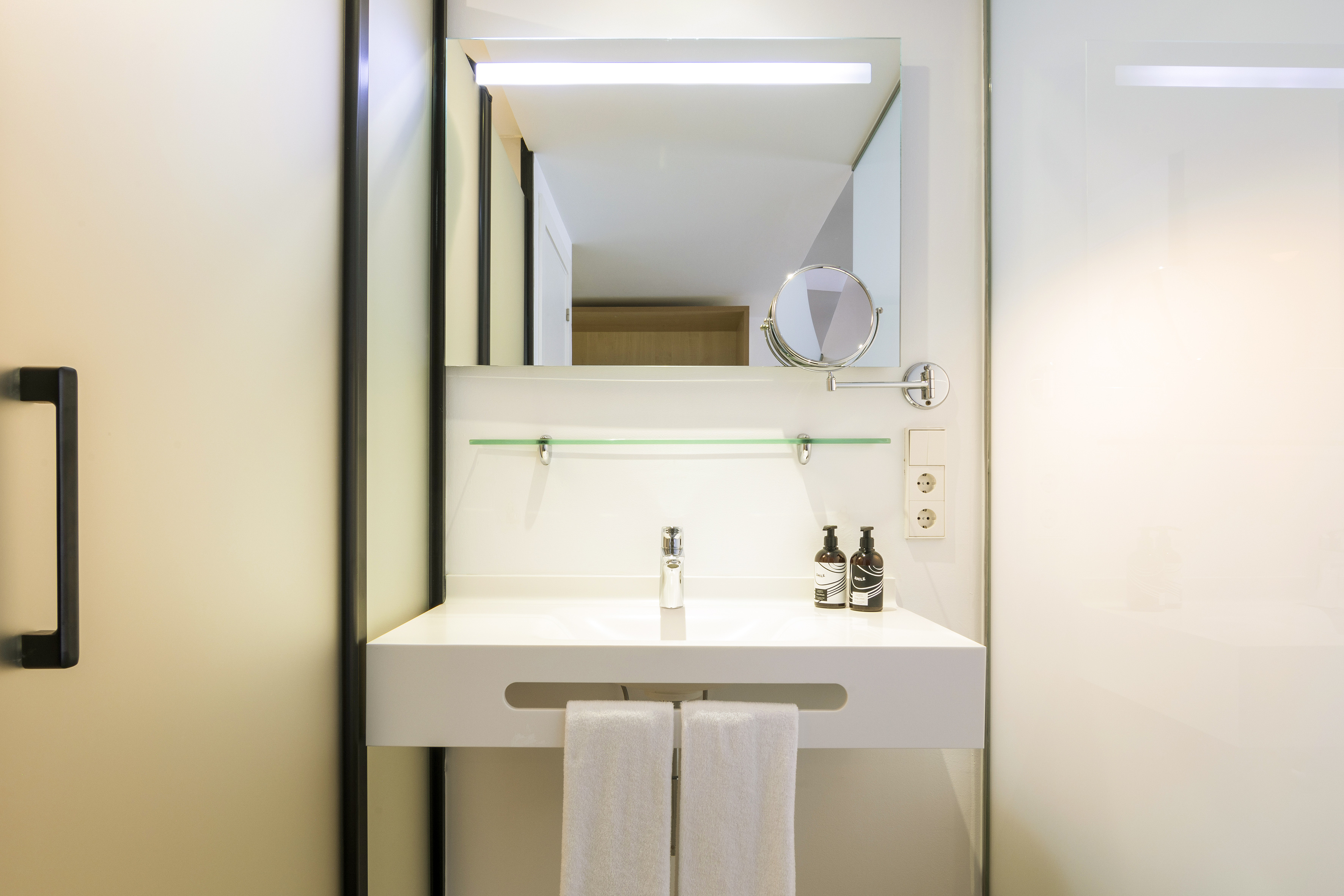Modern white bathroom vanity with integrated sink, lighted mirror, and towels.
