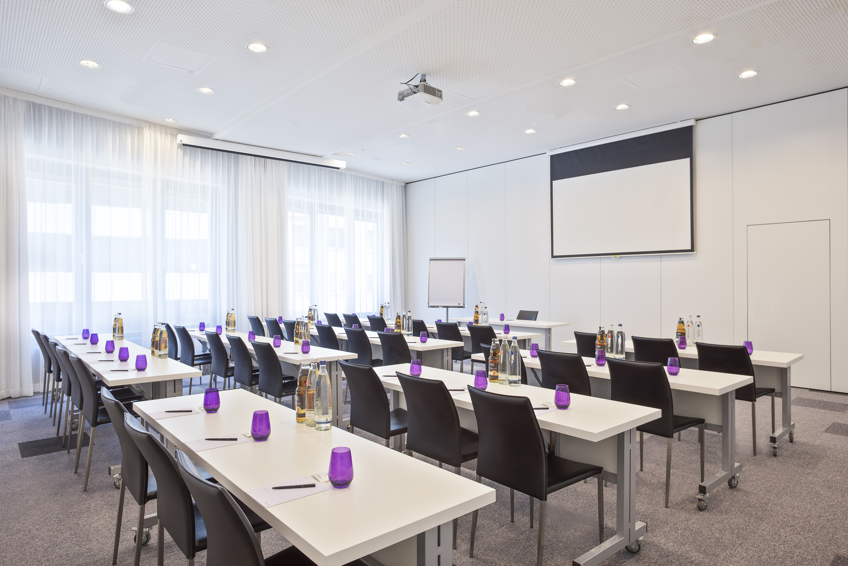 Modern conference room with tables, chairs, projector, and purple glasses.