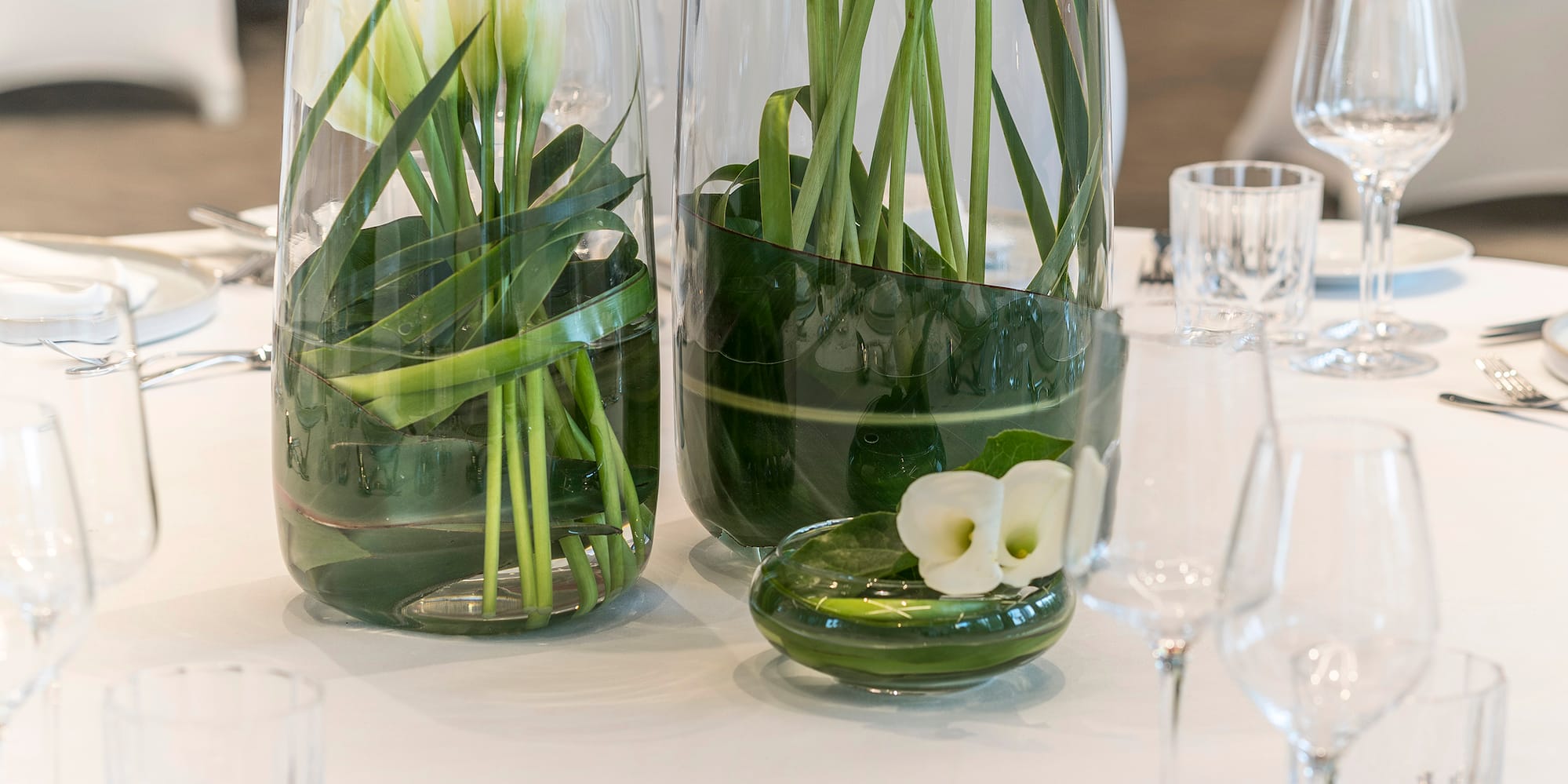 a table set with white and green vases with flowers