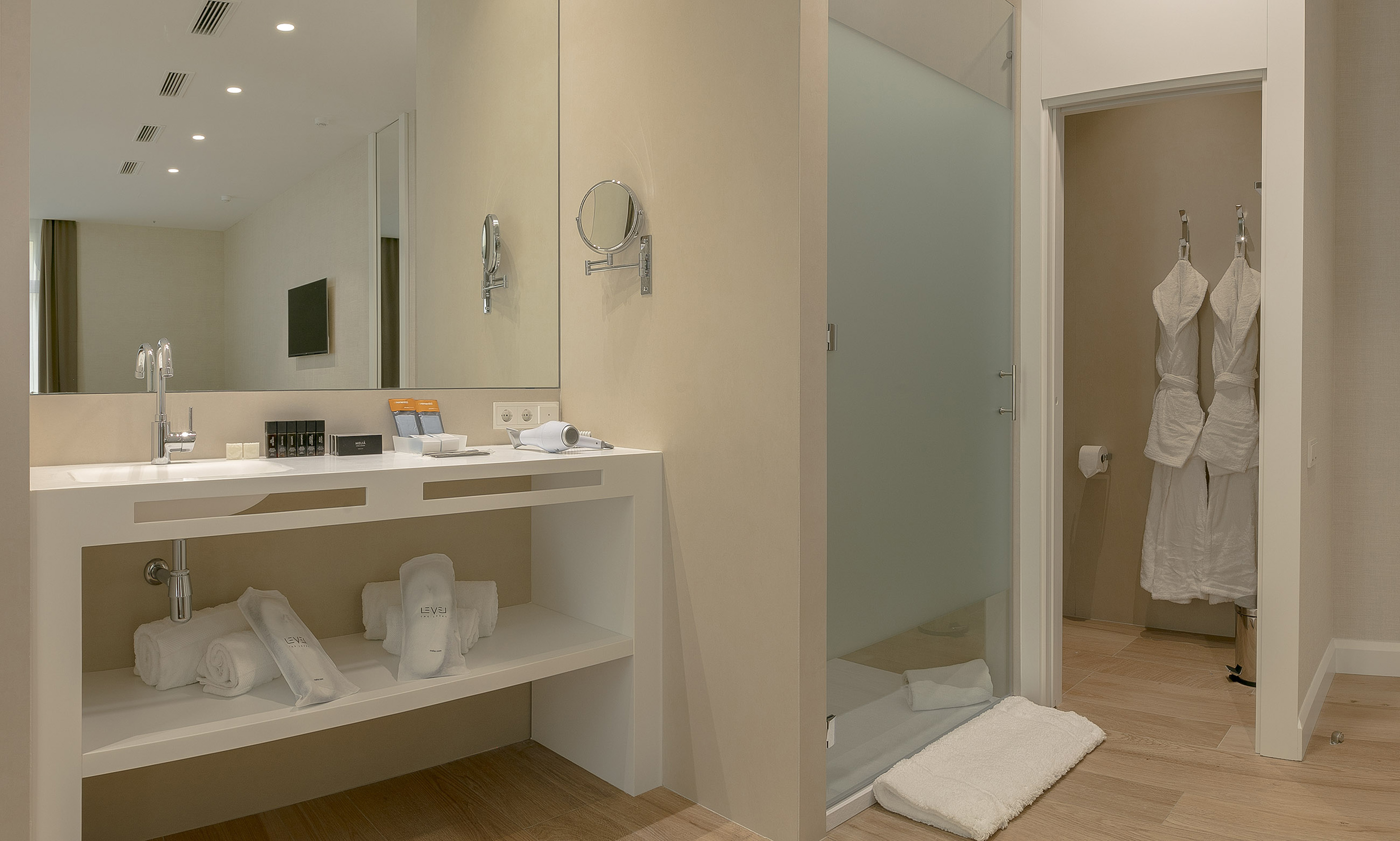 Modern hotel bathroom with double vanity, glass shower, and amenities.