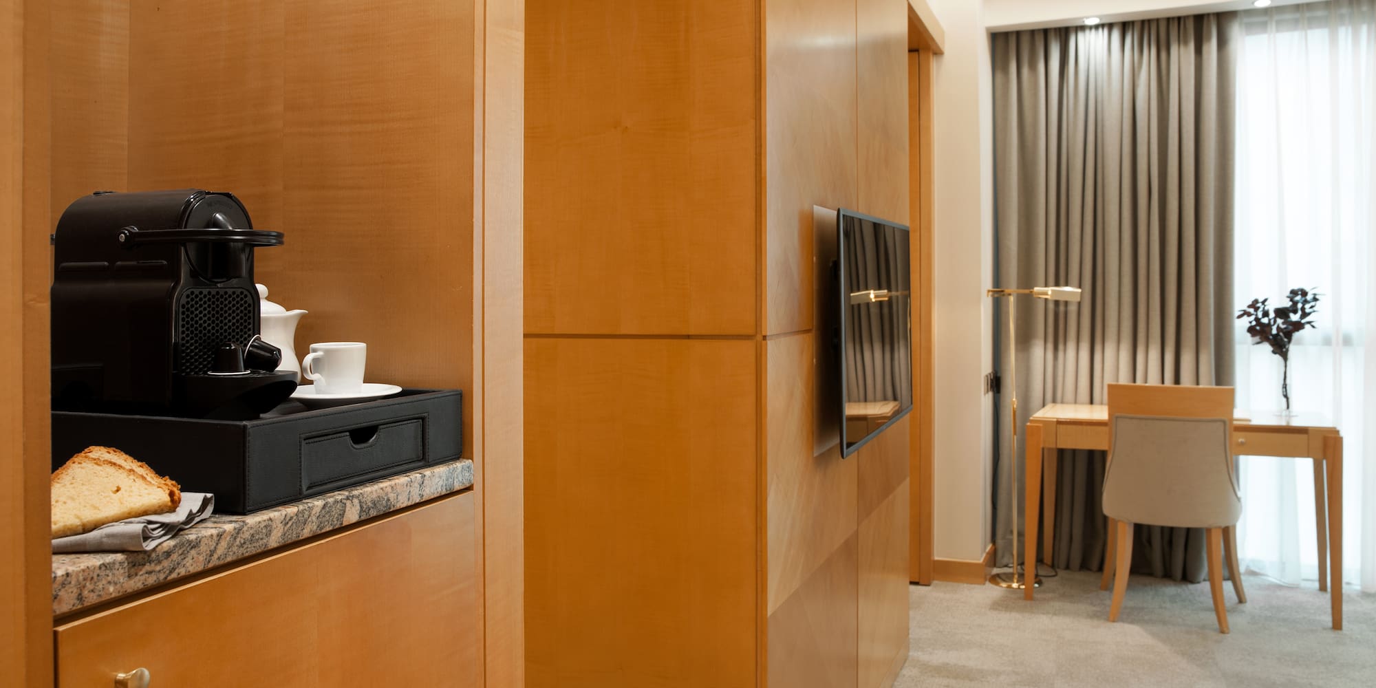 Modern hotel room with Nespresso coffee machine, wooden cabinets, desk, and TV.