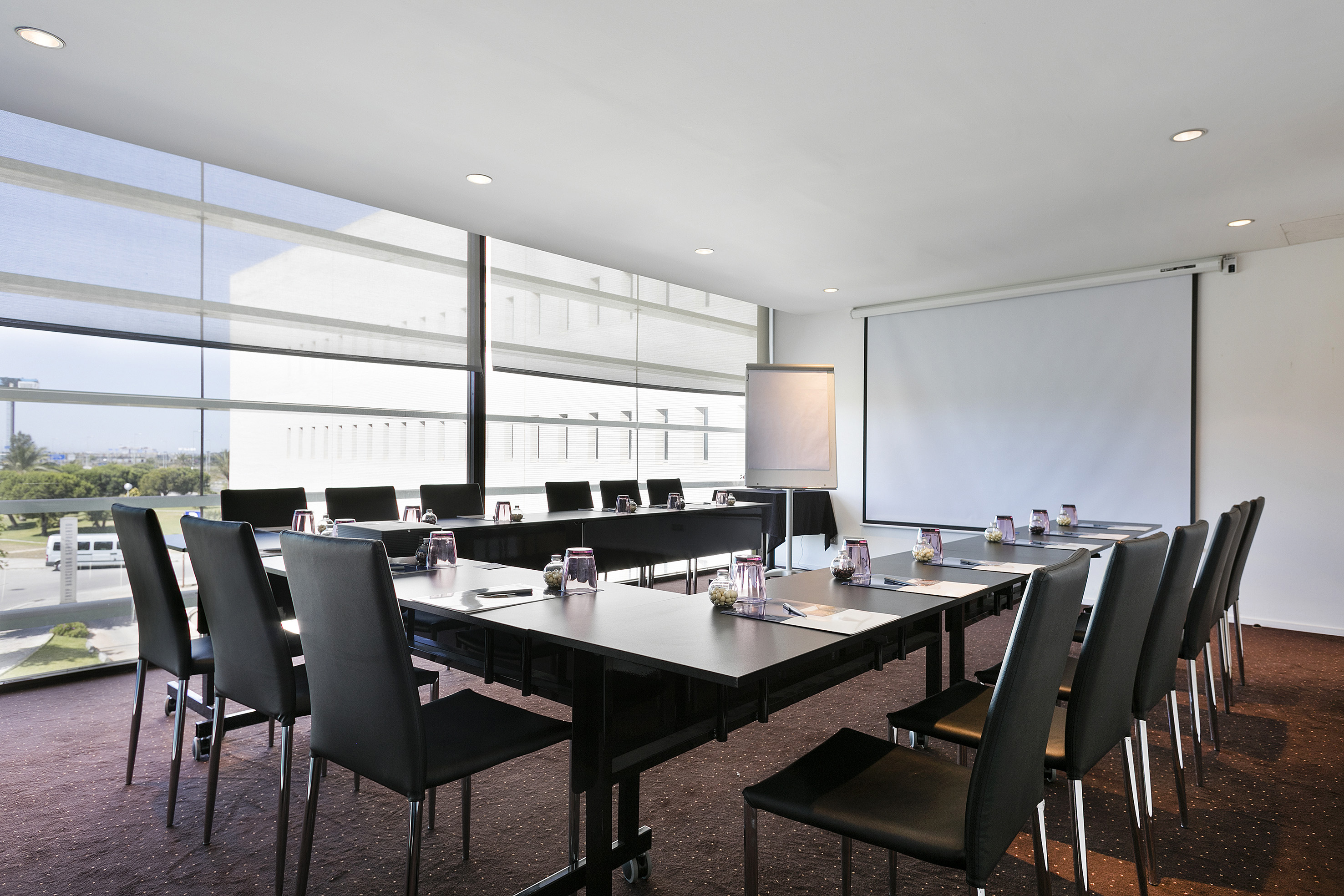 Modern business meeting room with U-shaped table, chairs, and projection screen.