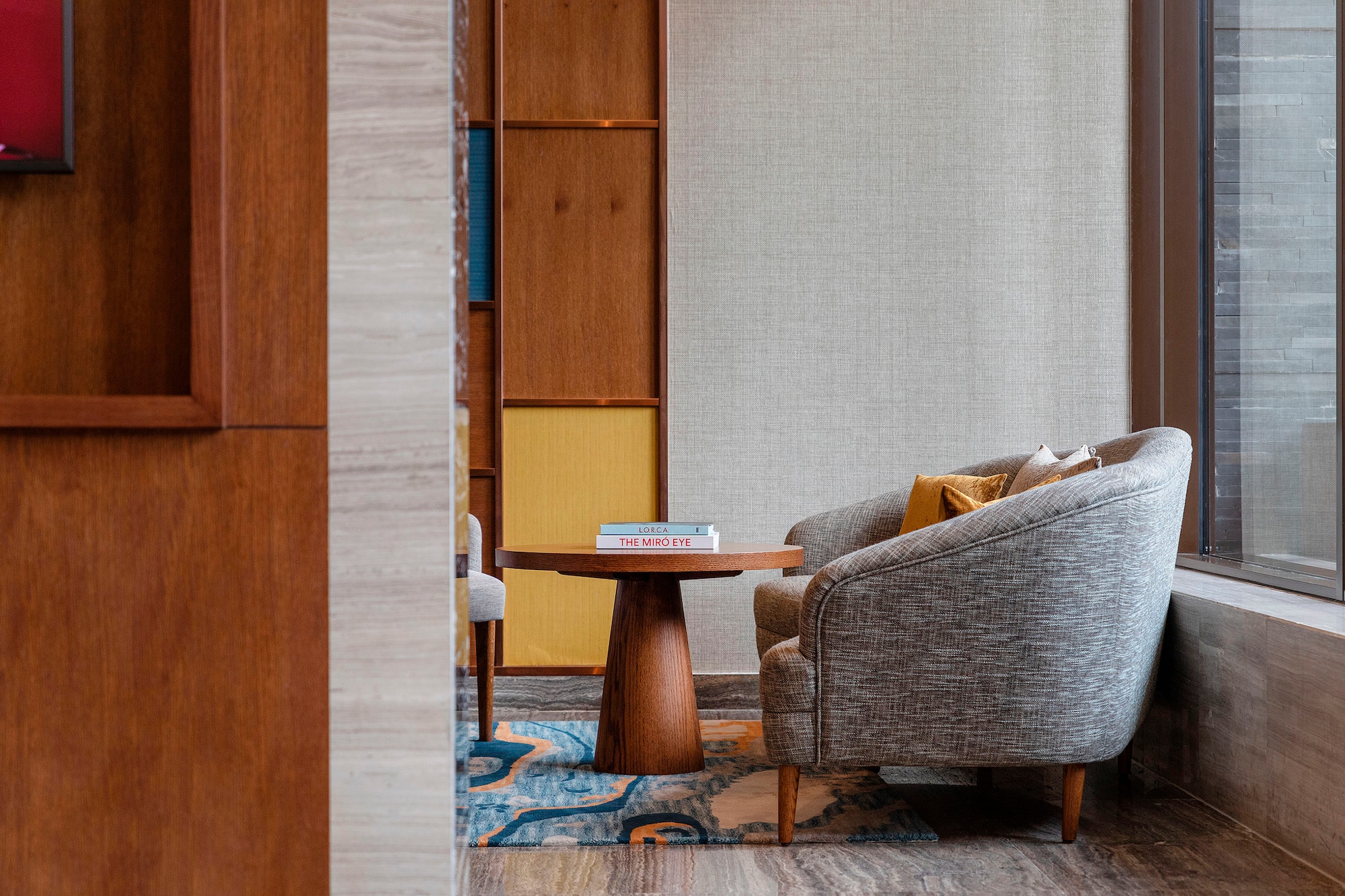 Hotel lounge with grey armchair, round wooden coffee table, and vibrant rug.