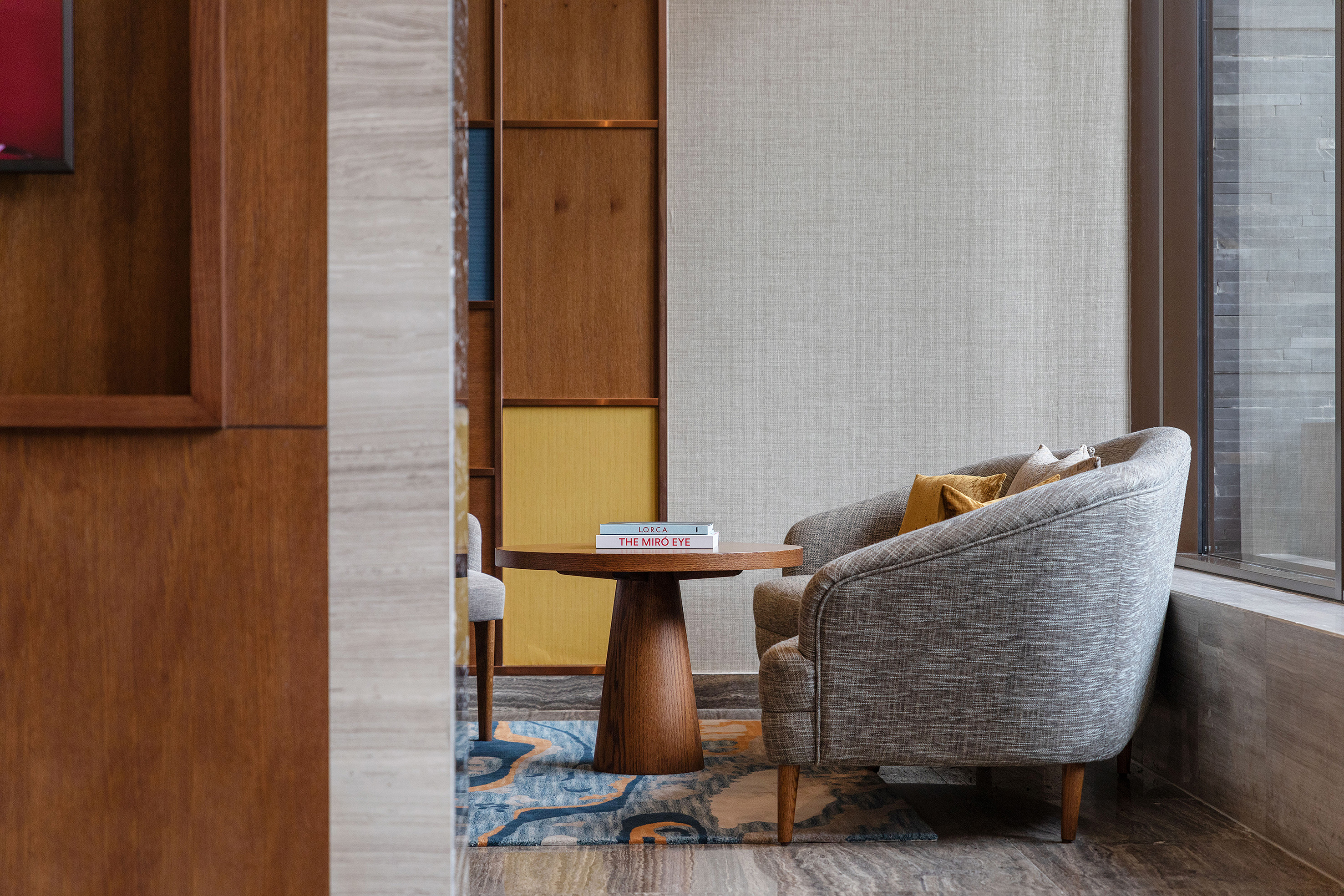 Hotel lounge with grey armchair, round wooden coffee table, and vibrant rug.