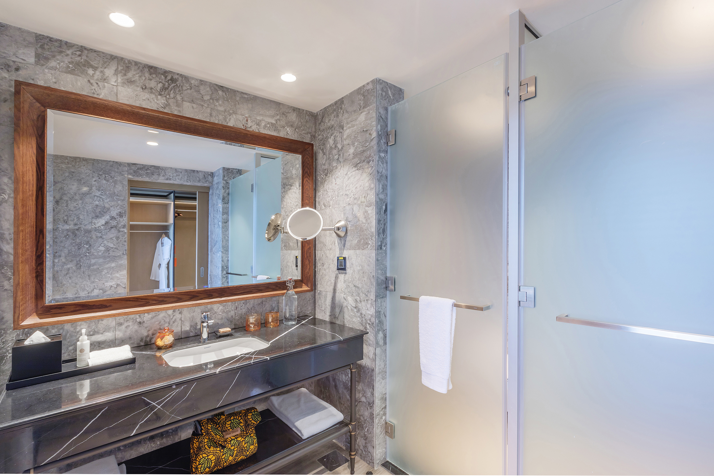 Modern hotel bathroom: black marble vanity, large mirror, frosted glass shower.