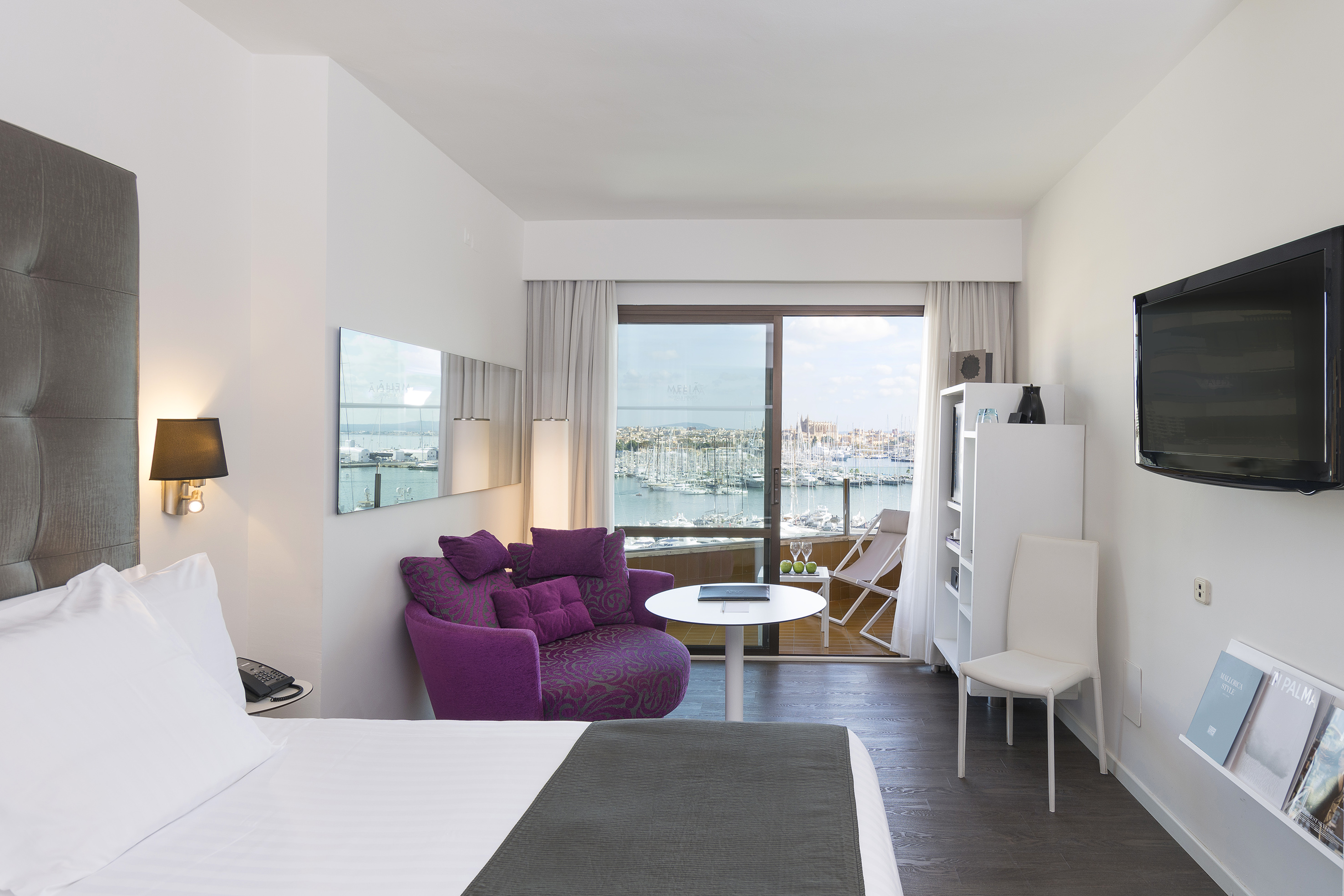 Modern hotel room with marina view balcony, bed, and cozy purple armchair.