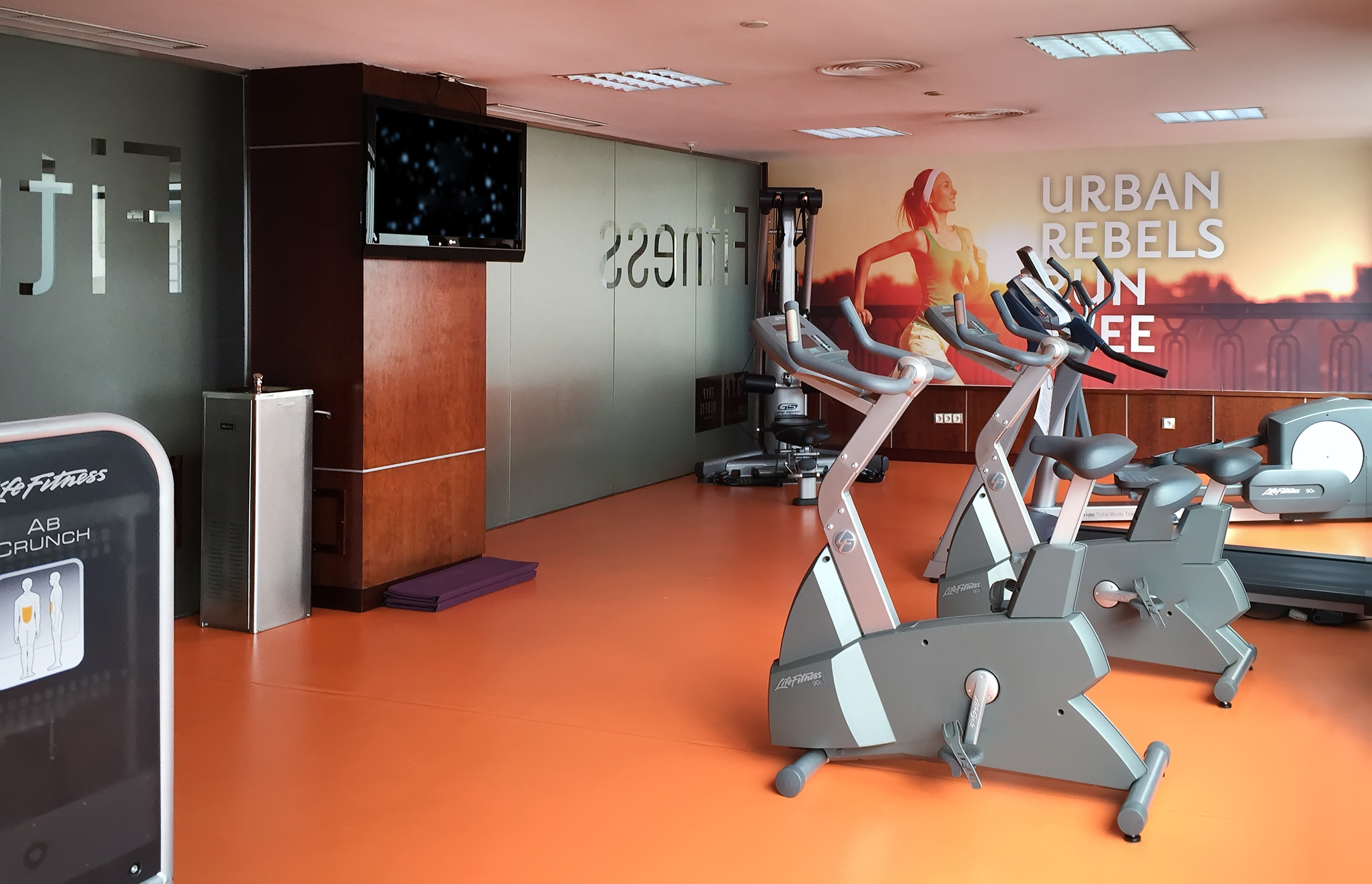 Gym with exercise bikes, treadmill, and vibrant orange floor.