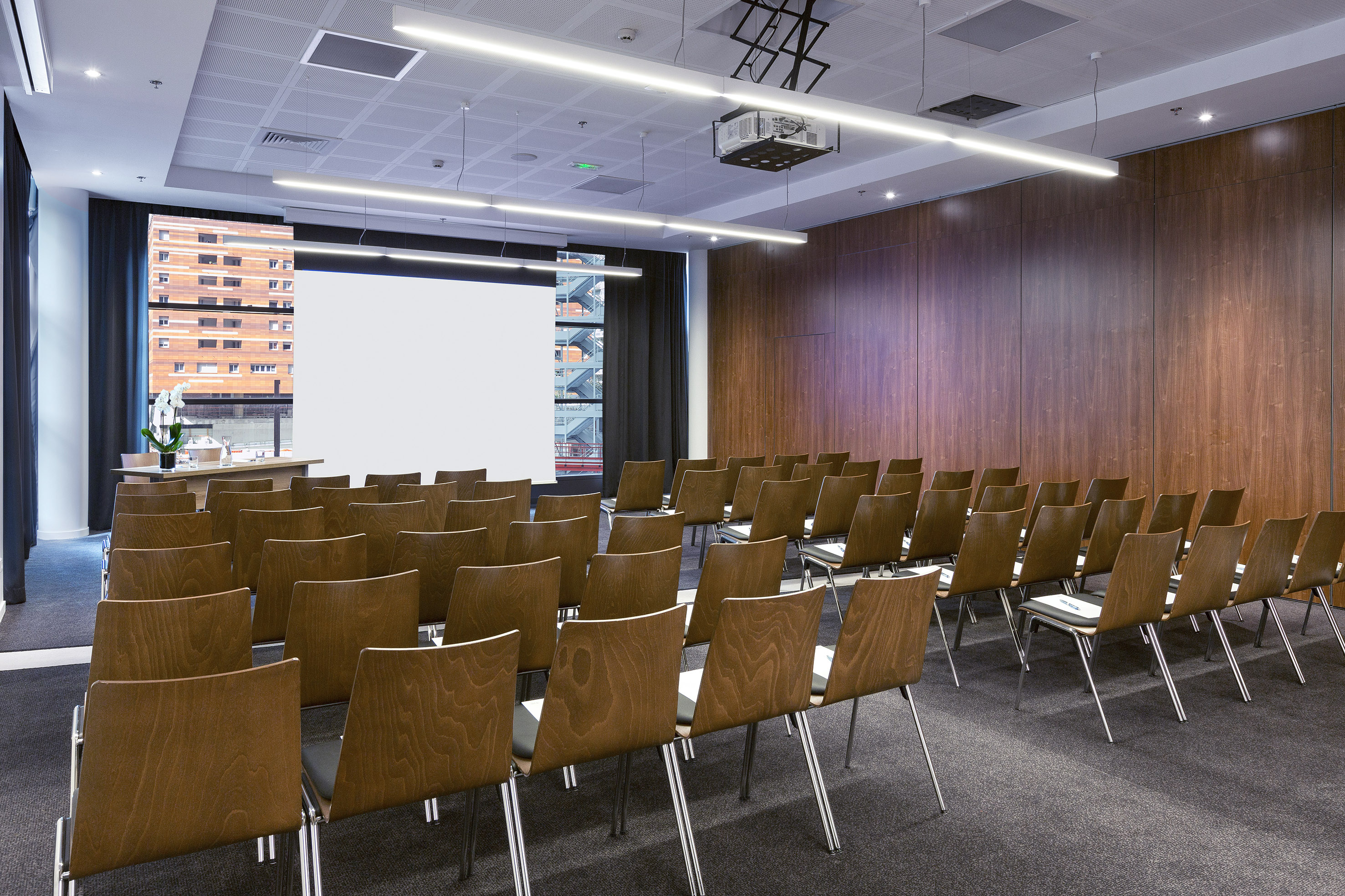 Modern conference room with wooden chairs, projector screen, and wood paneling.