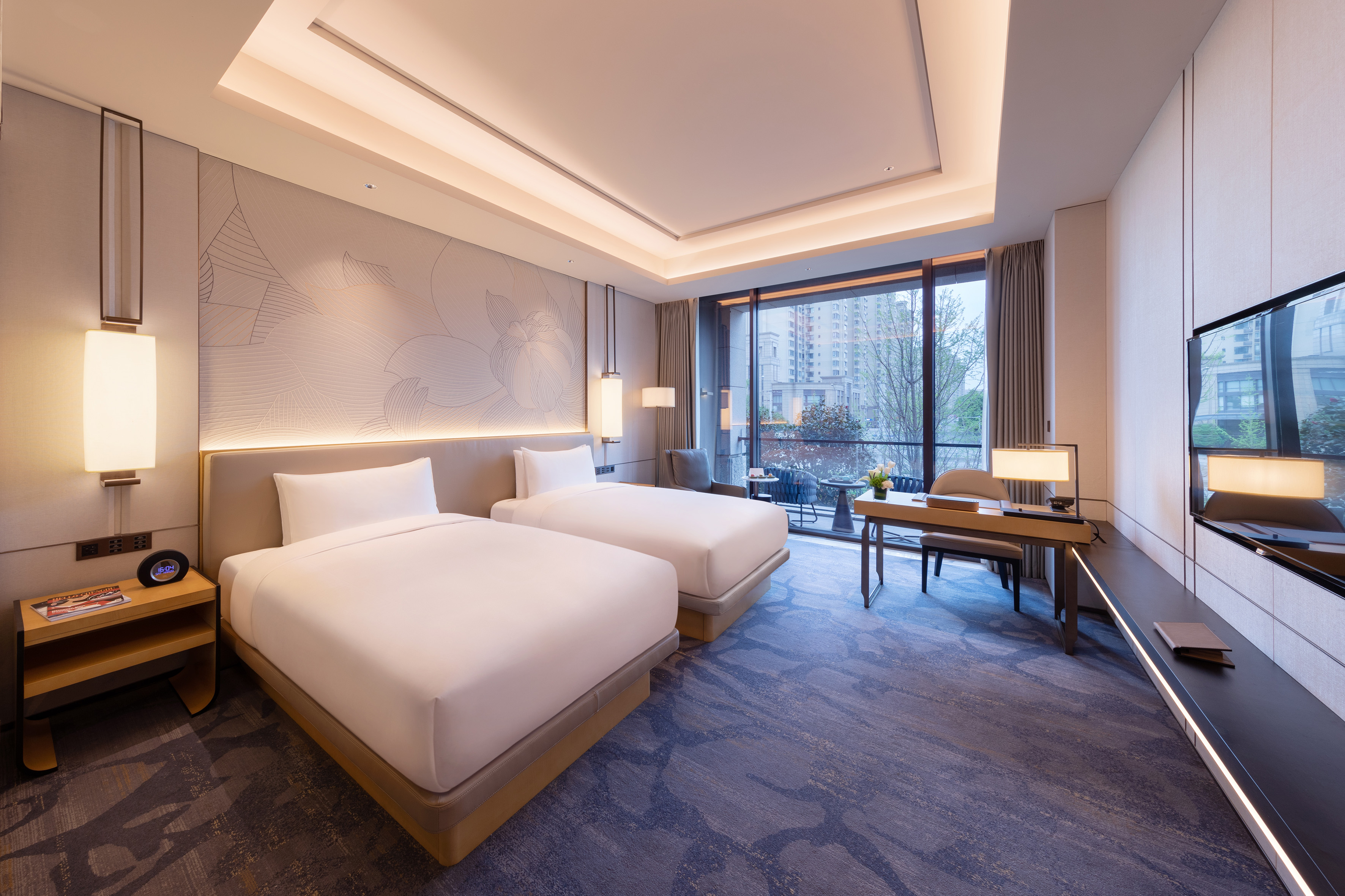 Modern hotel room with two twin beds, desk, balcony, and city view.