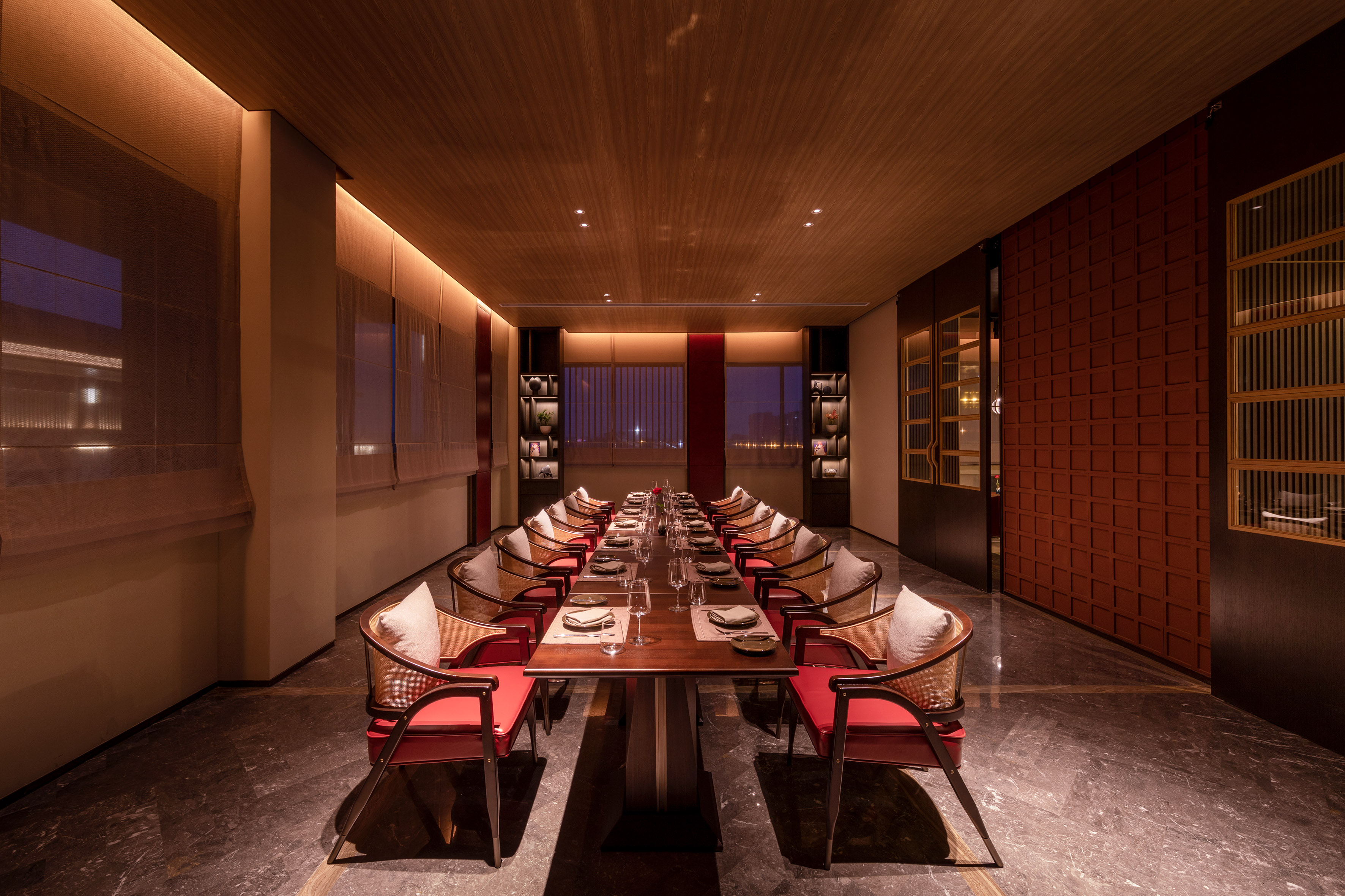 Elegant private dining room with long table, red chairs, warm lighting.