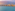 Dense urban skyline along a wide beach and calm sea, hazy morning light.