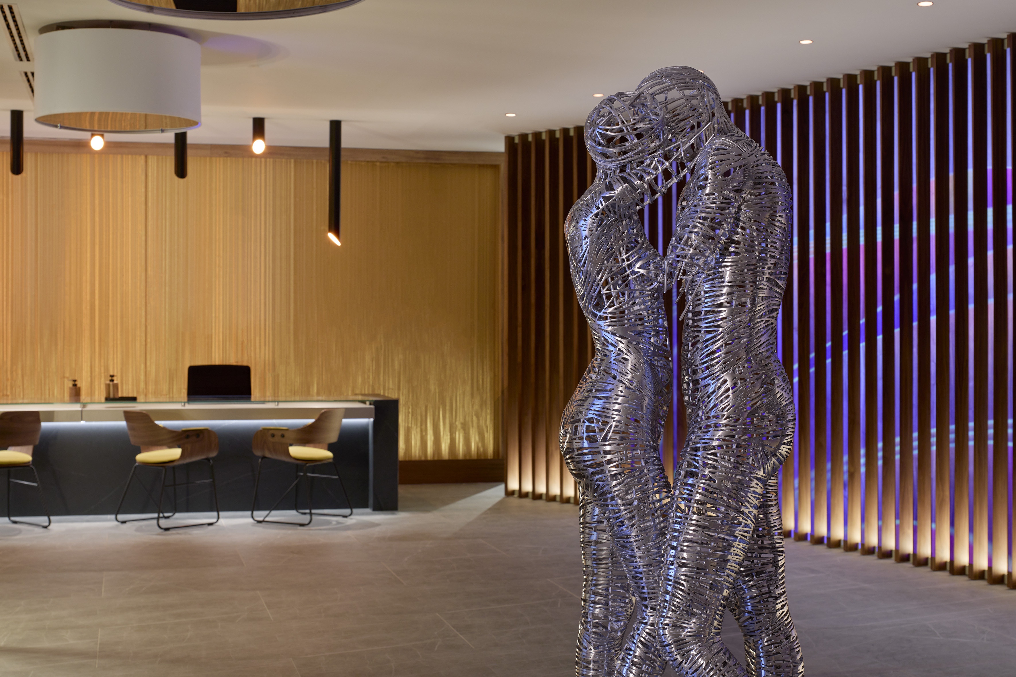 Abstract metal sculpture in modern lobby with gold walls and purple lighting.