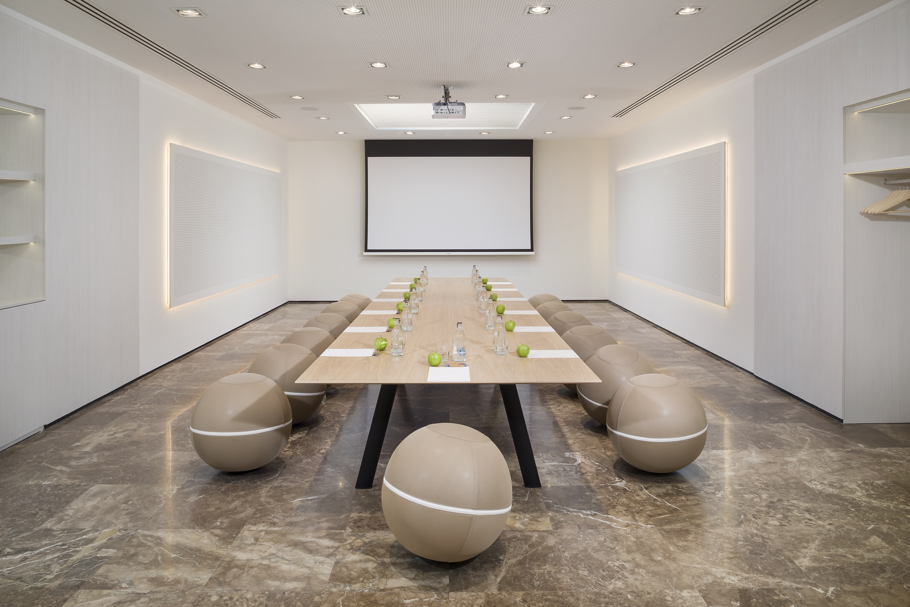 Modern conference room with long table, spherical seating, and projector screen.