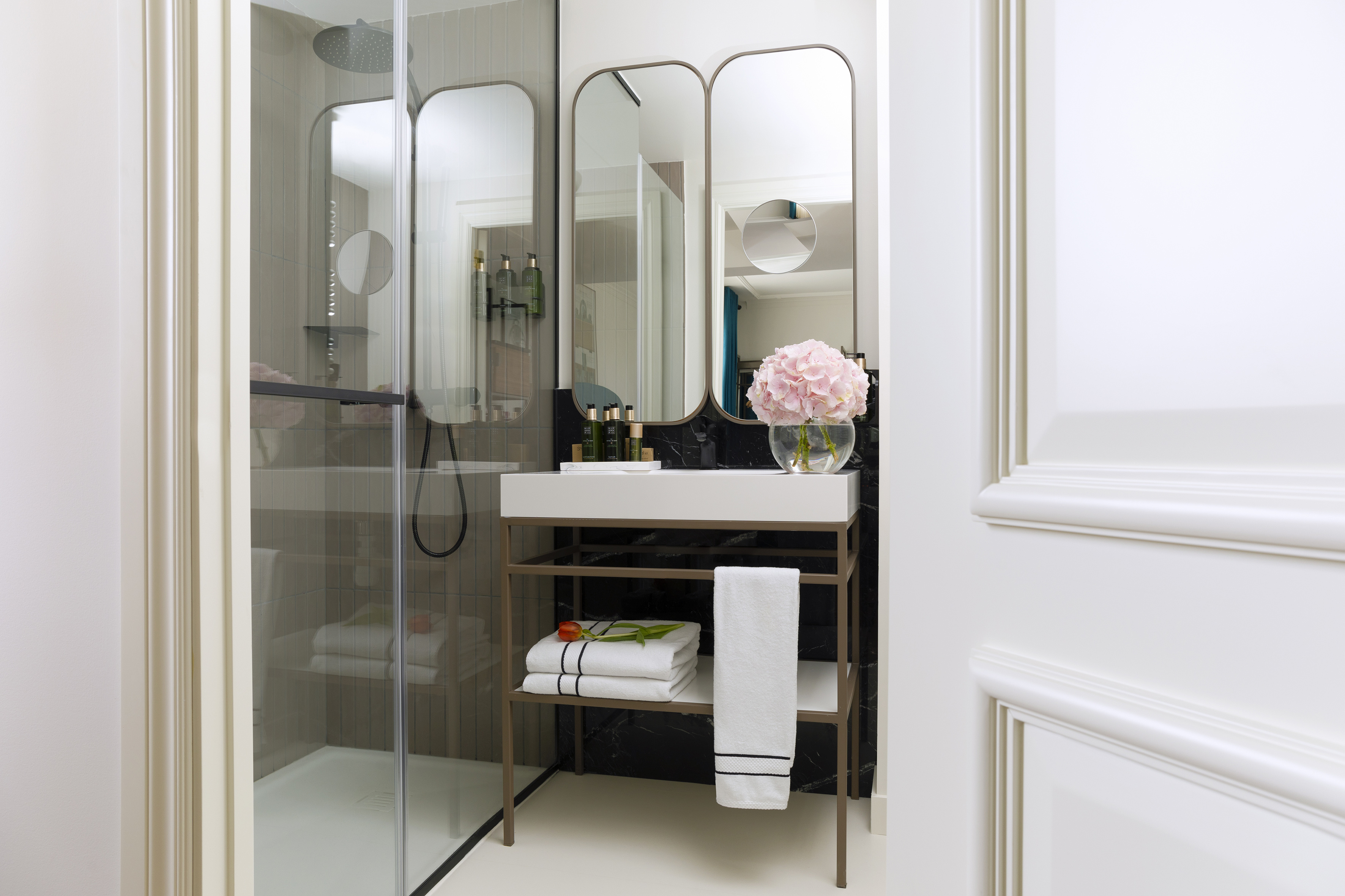 Modern bathroom with glass shower, vanity, double mirrors, and pink hydrangea.