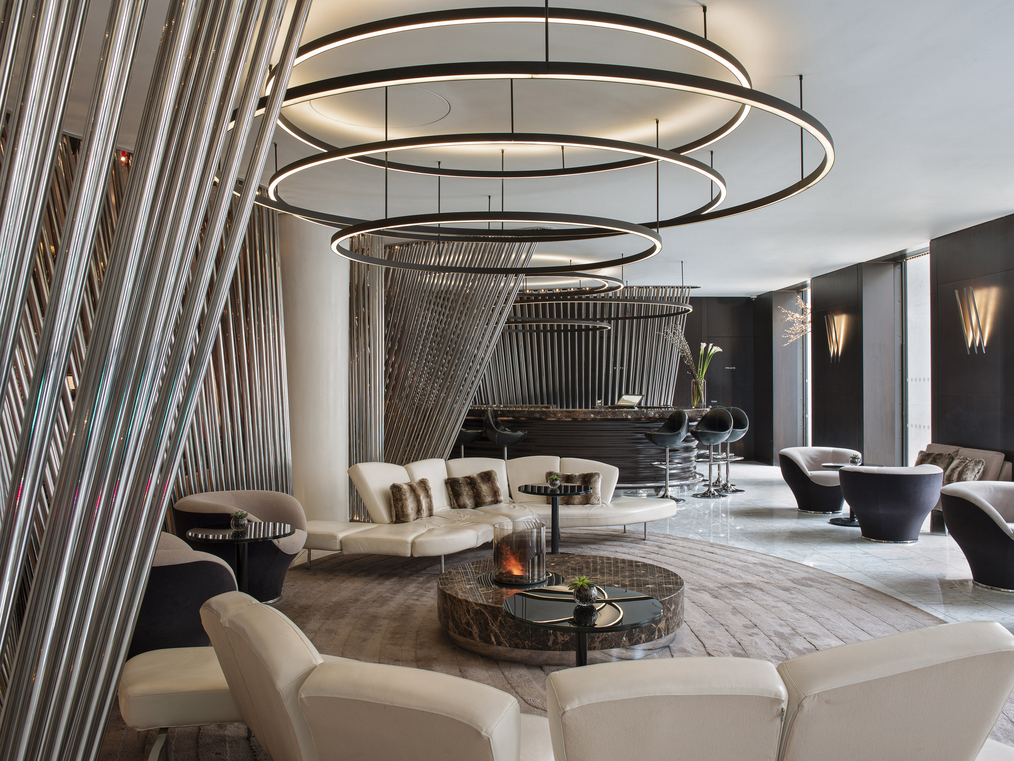 Modern lounge bar with circular LED lighting and curved white sofas.