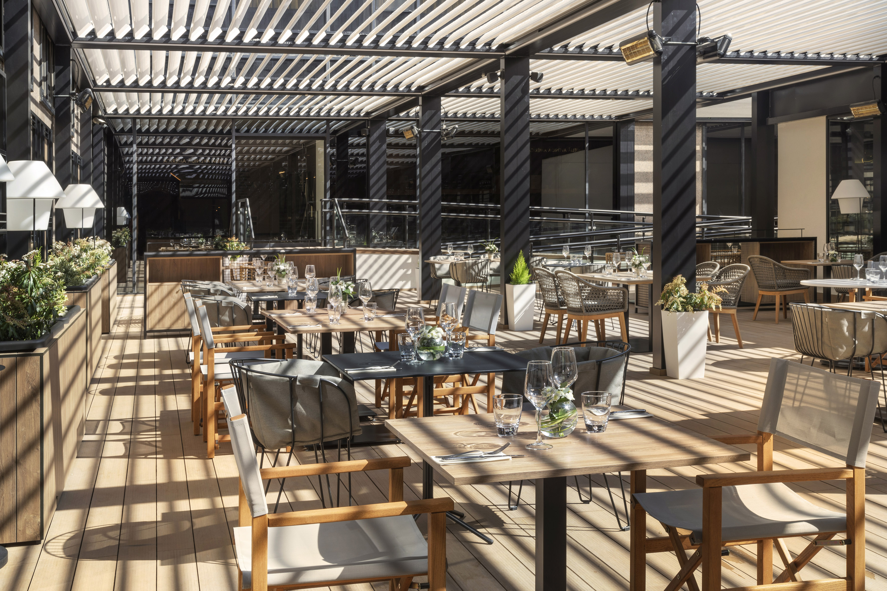 Upscale outdoor dining patio with modern tables, chairs, and slatted pergola.