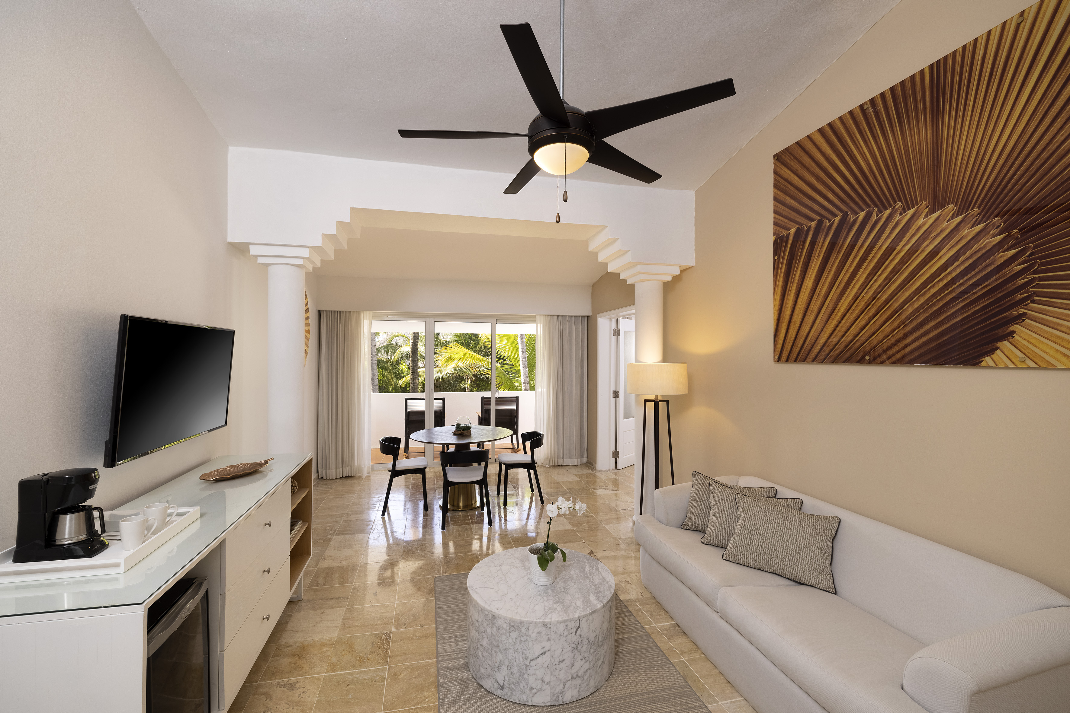 Modern hotel suite living room and dining area with balcony view.