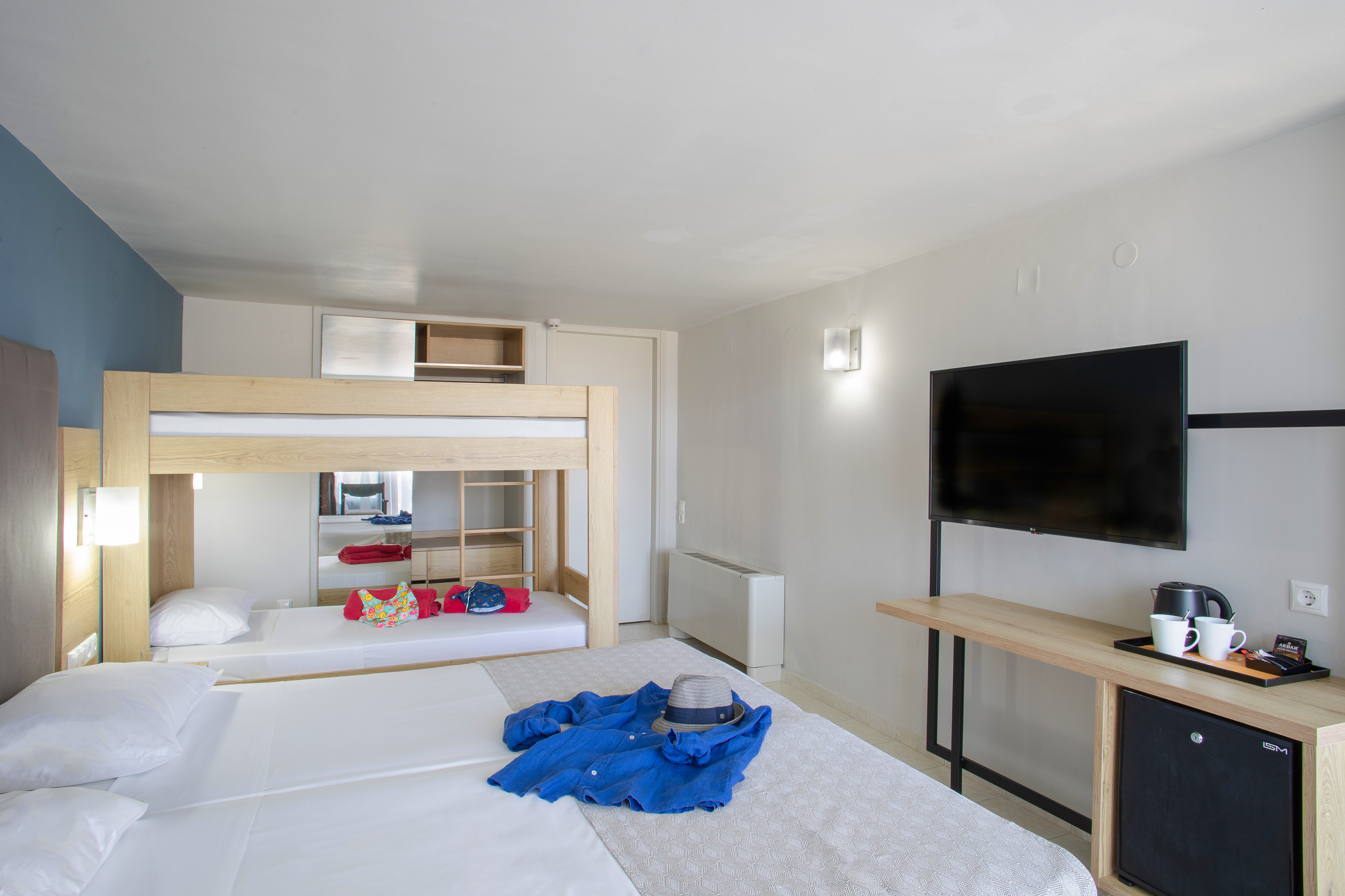 Modern family hotel room with bunk beds, double bed, TV, and mini-fridge.